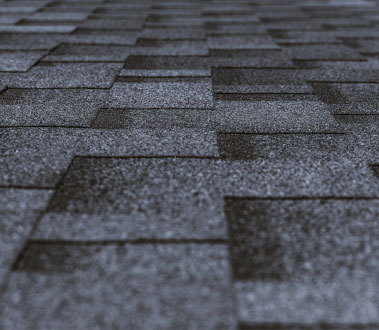 The image shows a close-up view of a roof with shingles, displaying a pattern of interlocking tiles against a dark background.