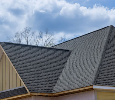 The image shows a roof under construction with visible shingles and a partially installed gutter system on a house during daylight hours.