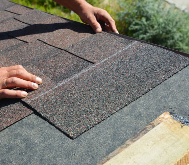 The image shows a person working on a roof, specifically applying a new layer of shingles to an existing roof with visible signs of wear or damage.