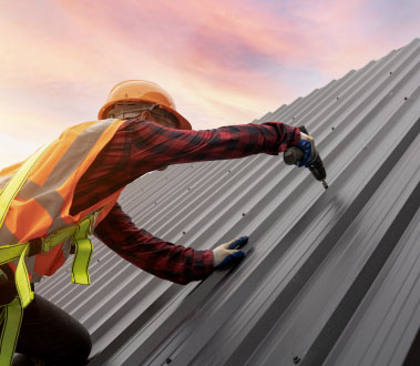 The image depicts a construction worker engaged in roofing work on a building, using tools and wearing safety gear.
