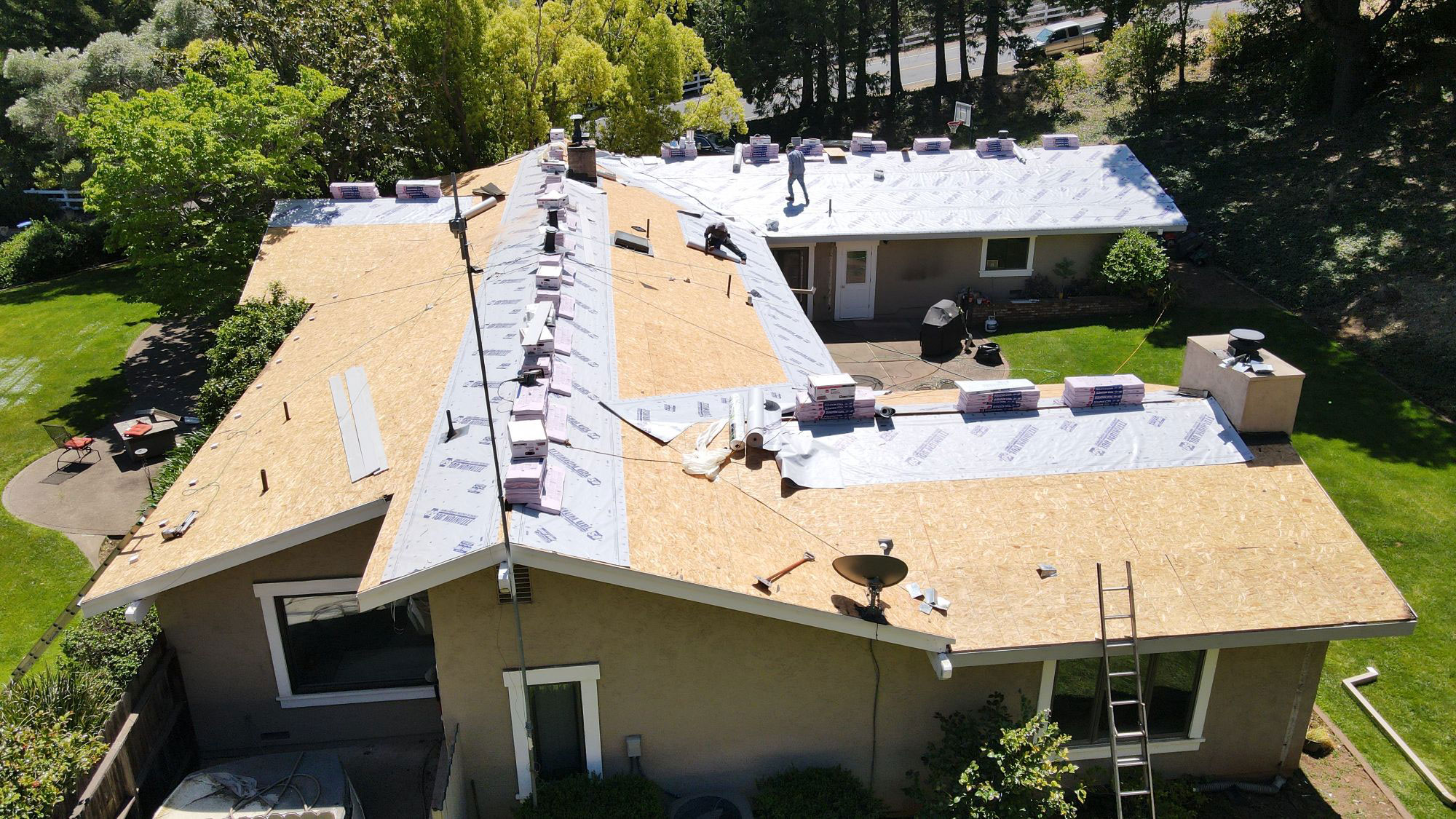 The image shows a residential house undergoing roof renovation with visible construction materials such as tarps and insulation installed on the roof.