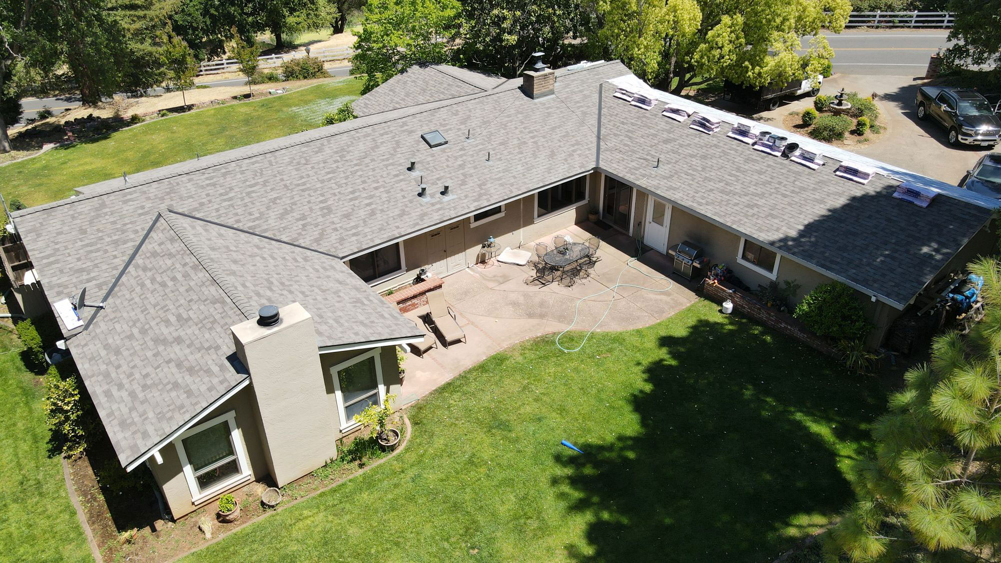 The image shows a single-story residential house with a pitched roof, a garage, and a backyard area on a clear day.