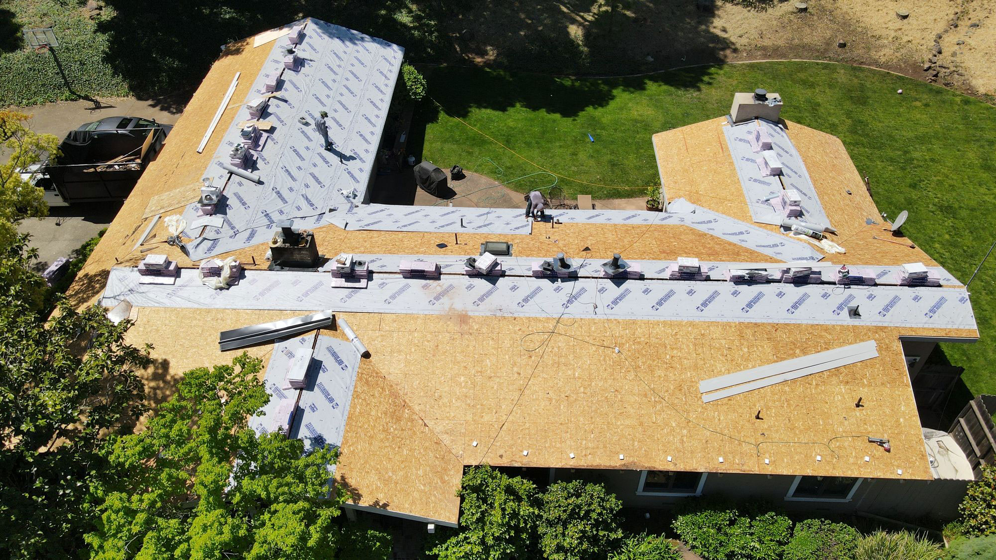 The image shows a house under construction with its roof covered in tarps, indicating ongoing renovation work.