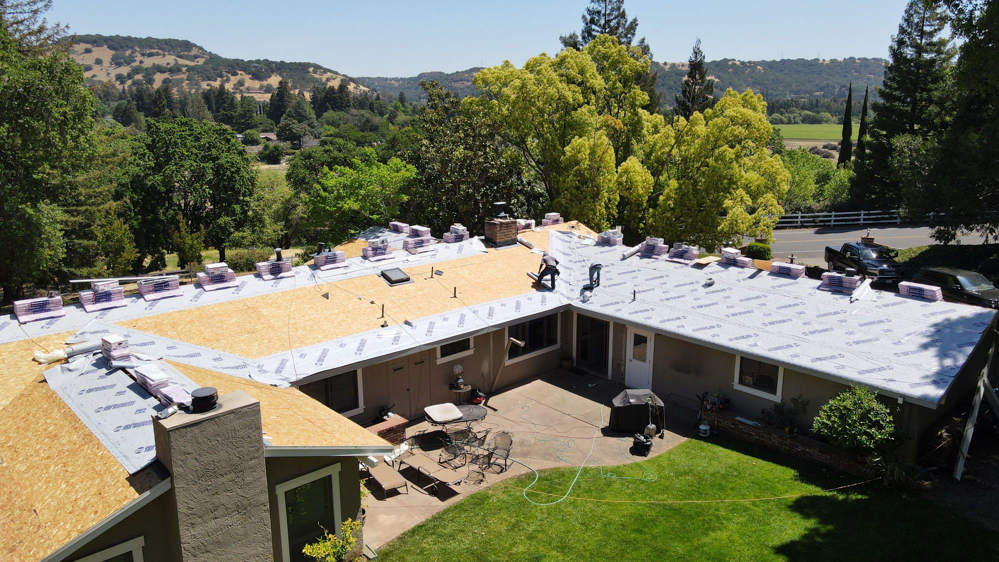 The image shows a house under construction with a visible roofing process, featuring a flat roof being prepared for installation.