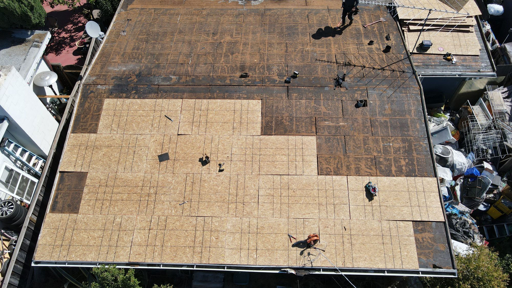 The image shows a roof under construction with exposed wooden planks and tarps covering the area.