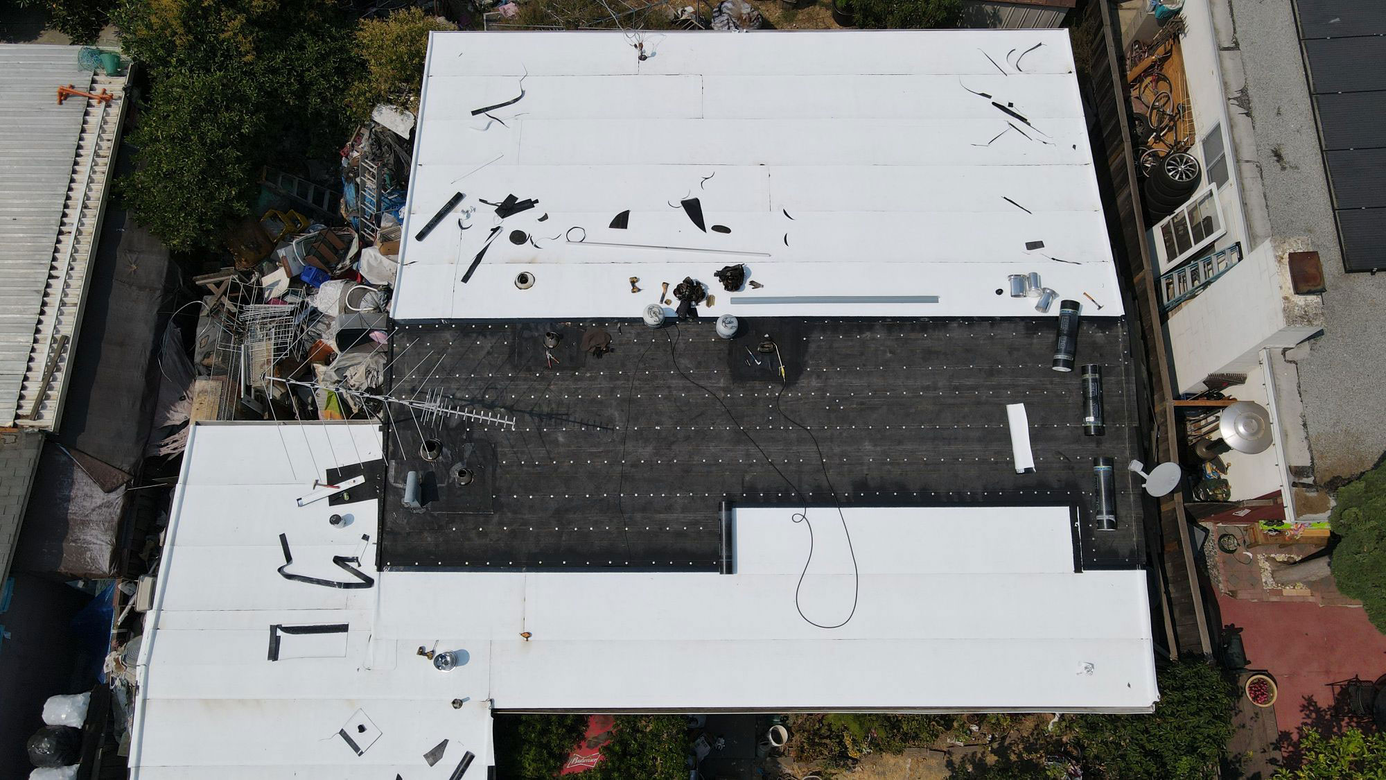 The image shows a large white building with a flat roof under construction or renovation, featuring exposed insulation and plywood panels.