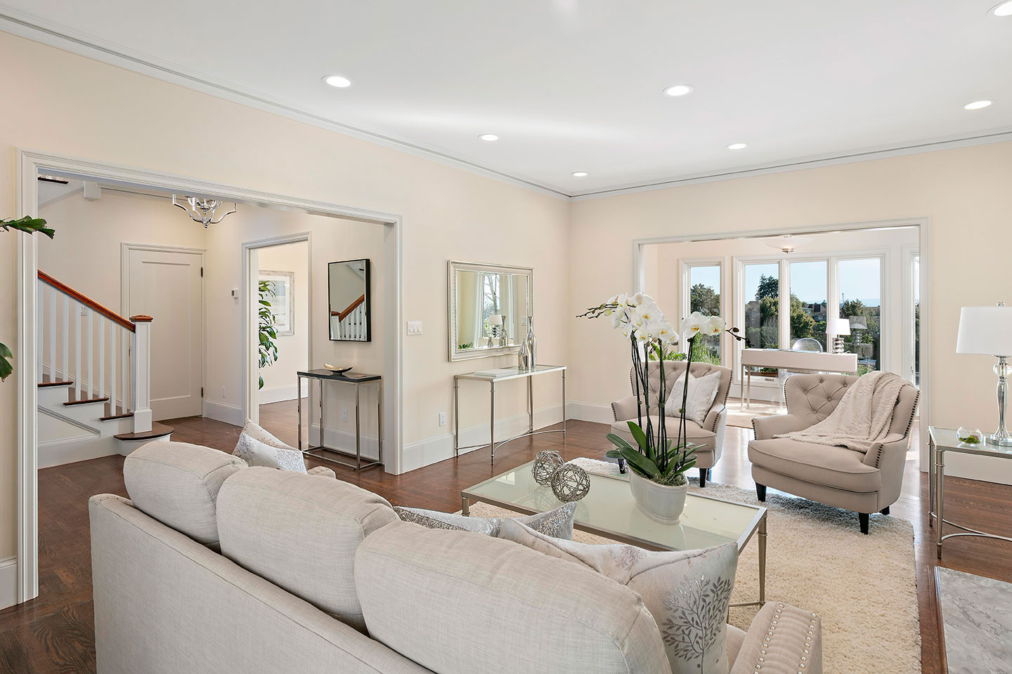 The image shows a modern living room with light-colored furniture and decor, featuring hardwood floors, a neutral color palette, and ample natural light.