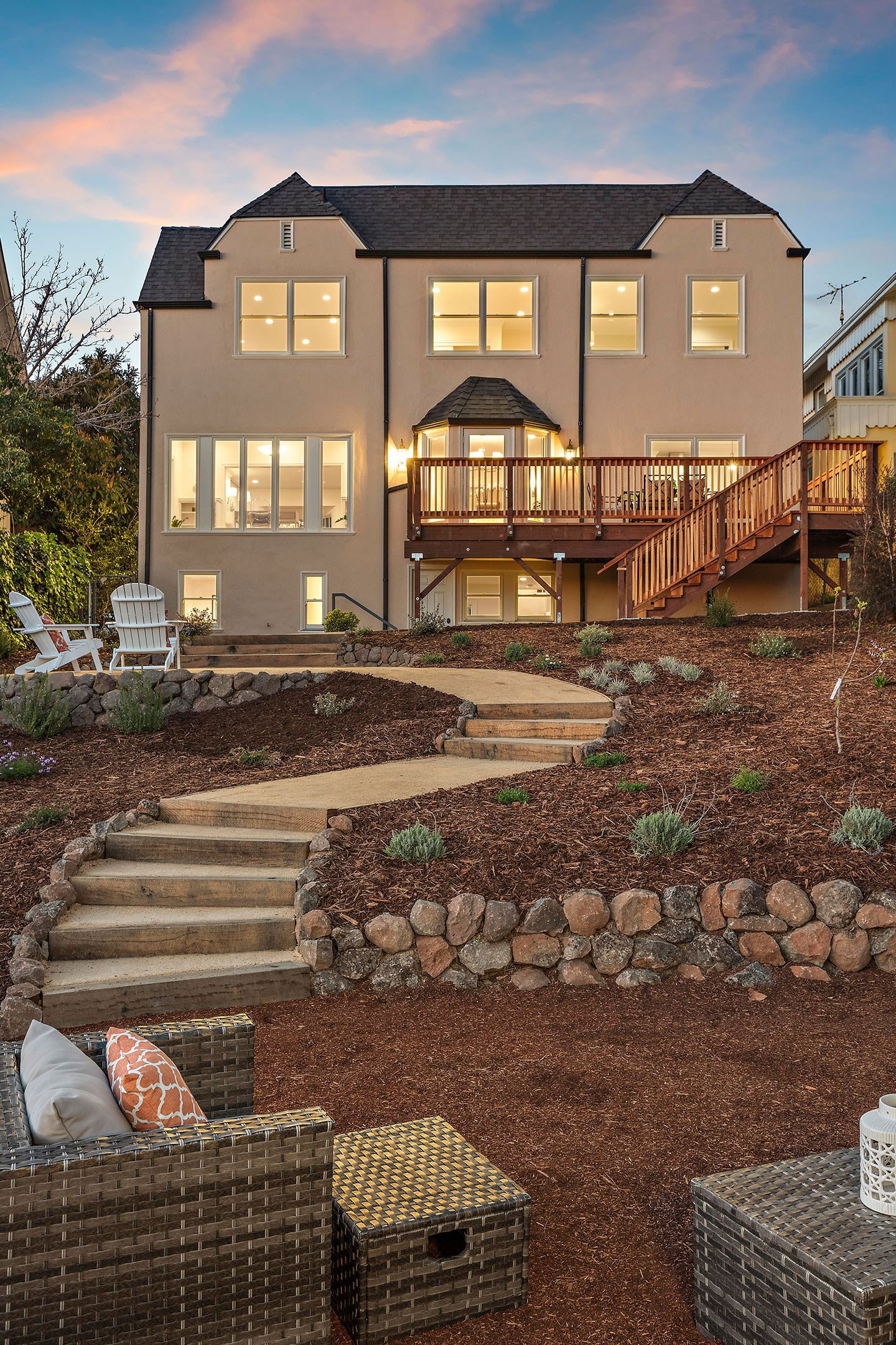 The image shows a two-story residential house with a prominent front porch, set against a backdrop of dusk sky.
