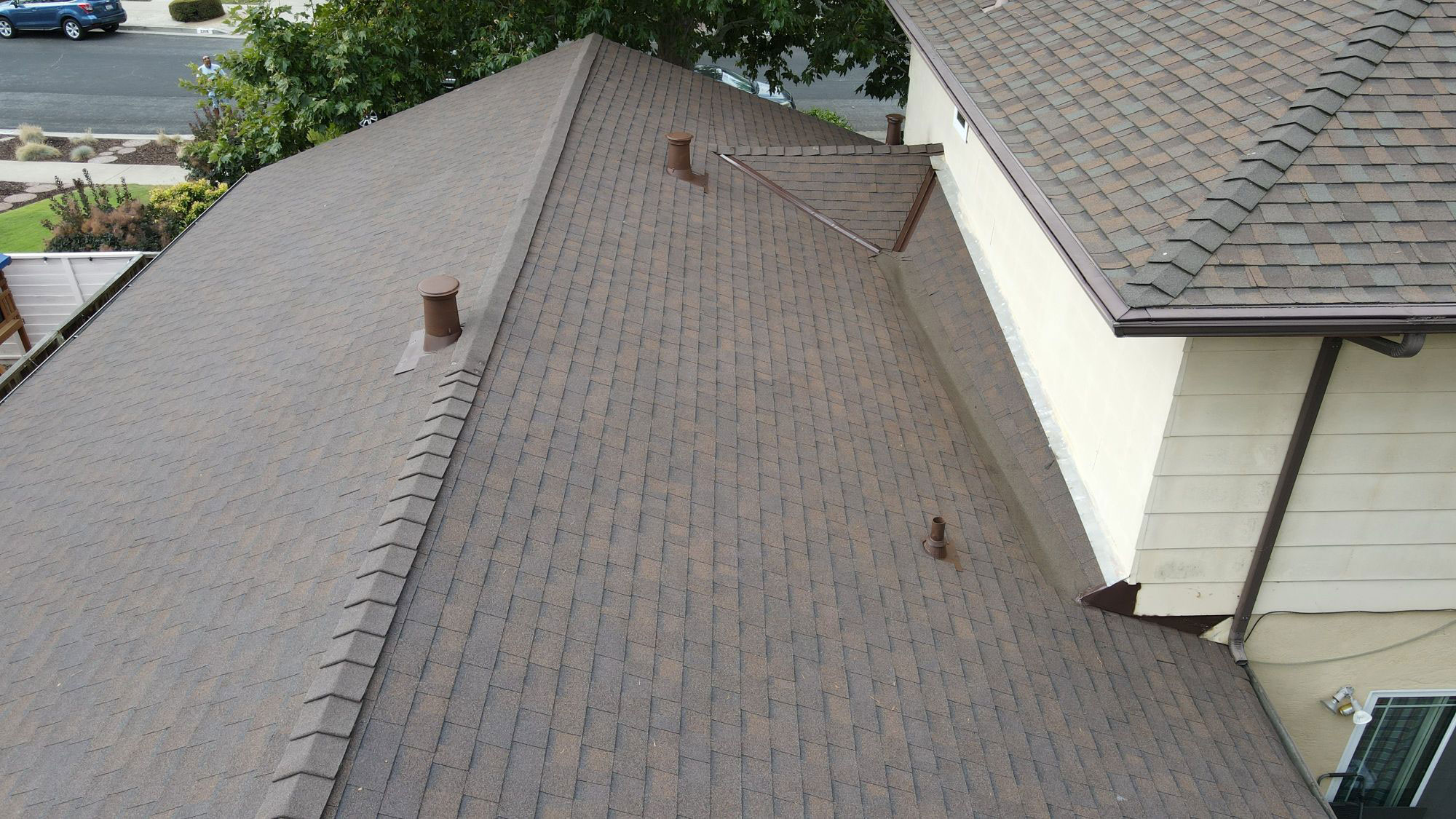 The image shows a residential house with a dark brown shingle roof, featuring multiple layers and varying textures.