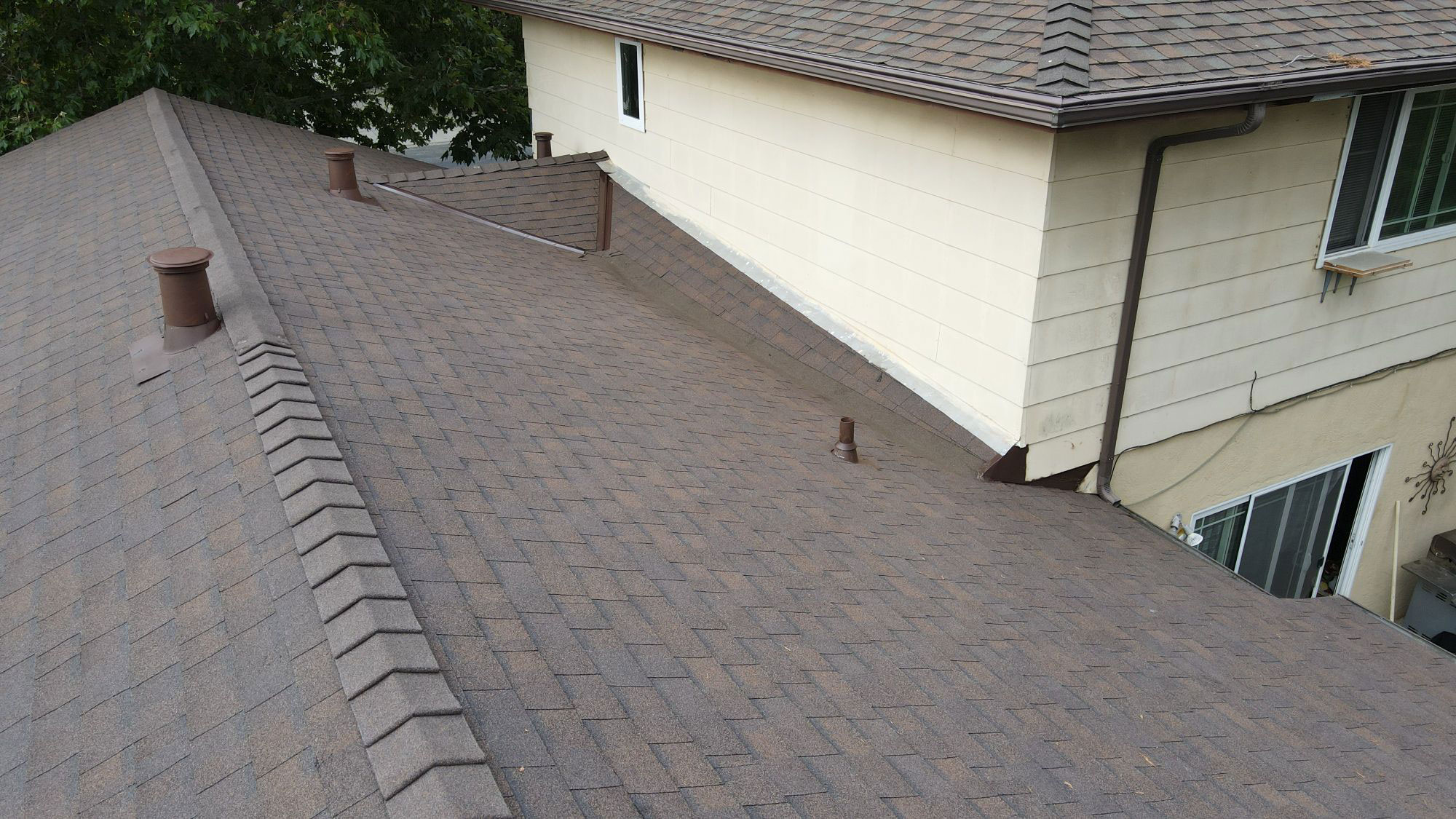 The image shows a section of a residential roof with shingles, featuring a visible seam where two sections of the roof meet.