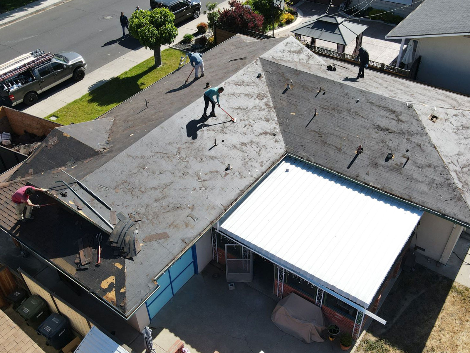 The image shows a roofing construction site with workers engaged in repairing a damaged roof.