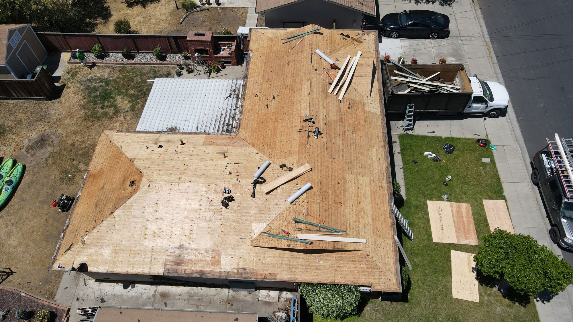 The image shows a building under construction with visible wooden studs, roofing materials, and tools on the ground, indicating ongoing work.