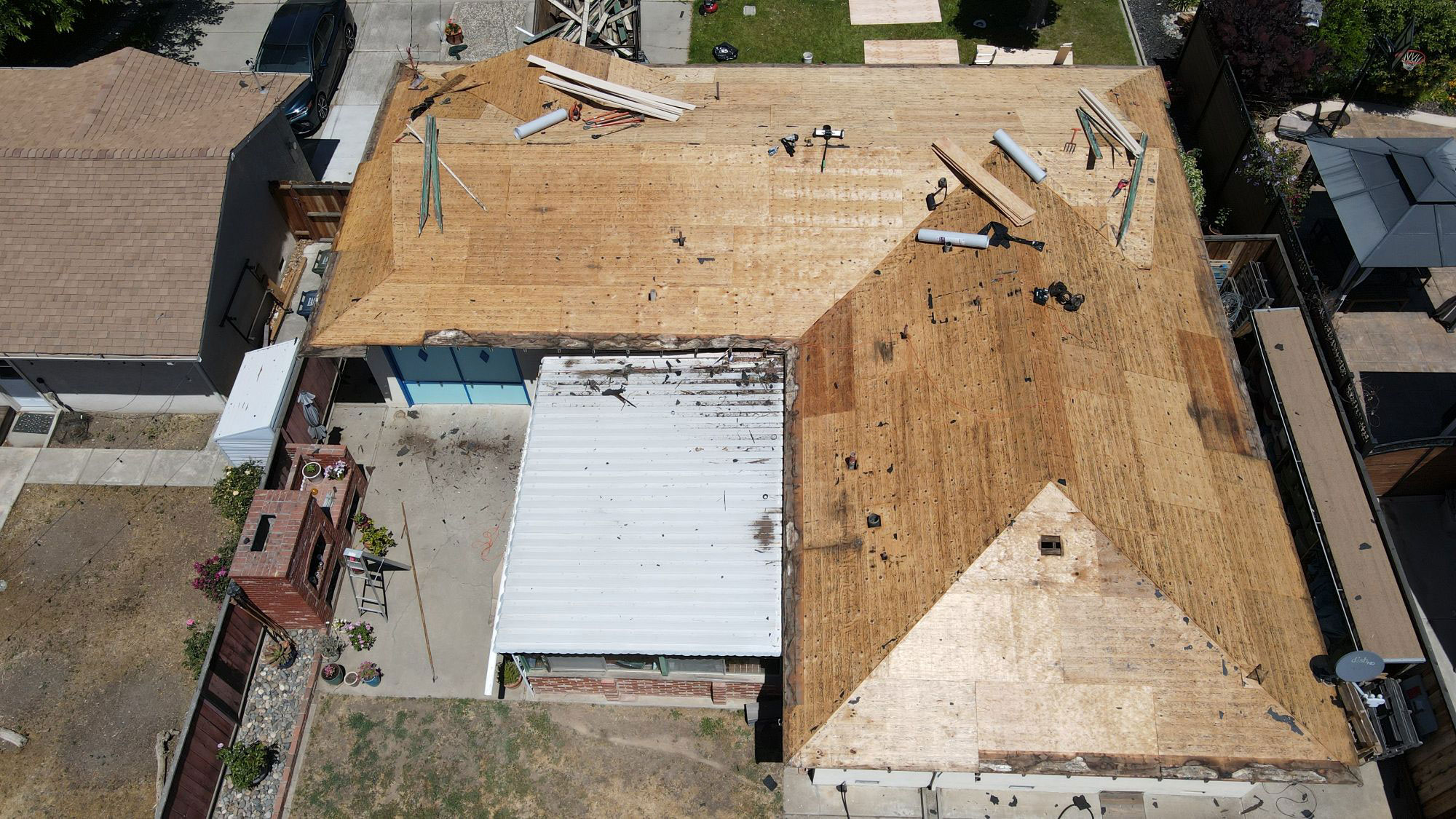 An aerial view showing a building with a damaged roof under repair, surrounded by a residential area with houses in the background.