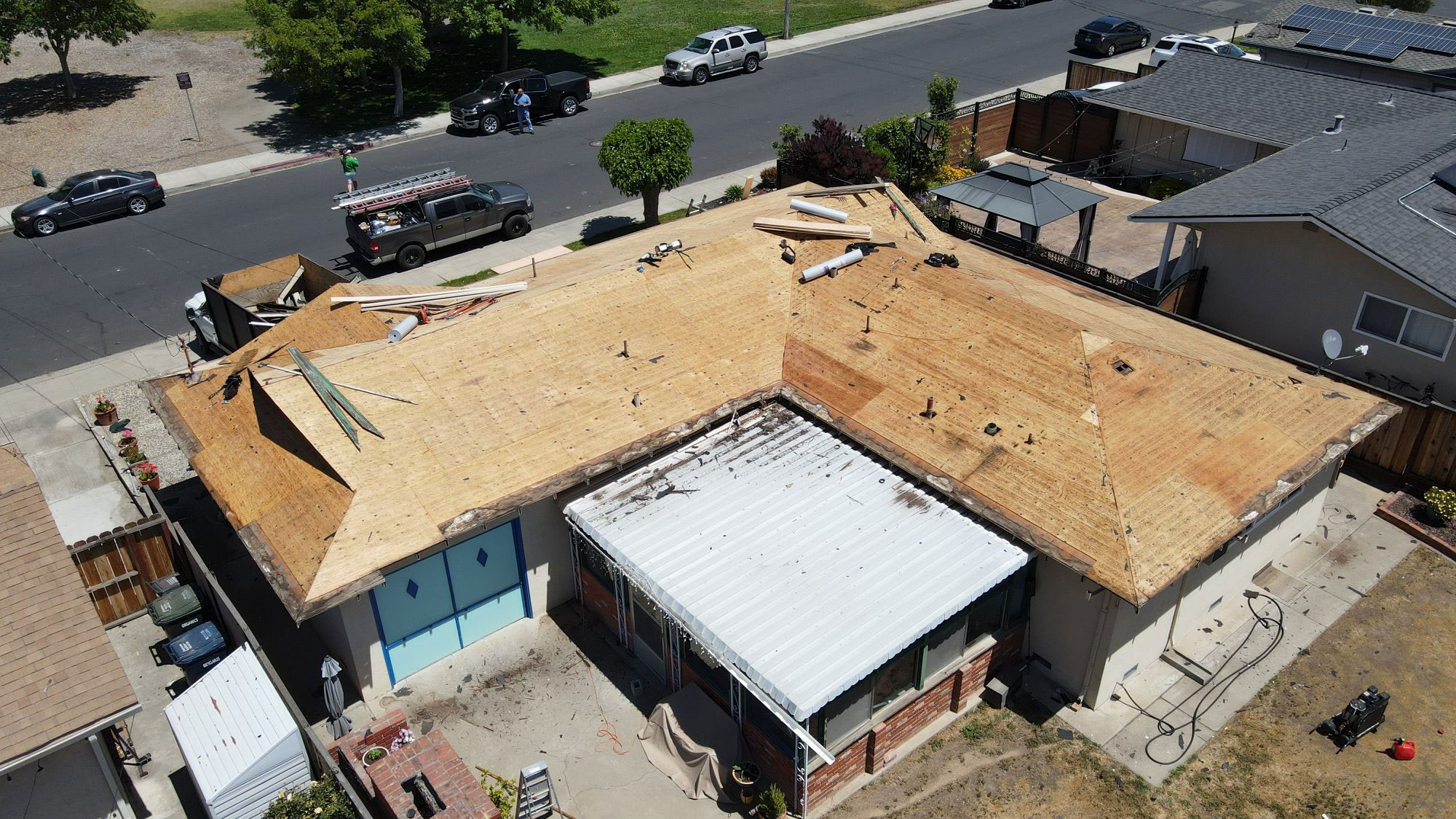 This is an aerial view of a residential house undergoing roof repairs with visible tarps on the roof.