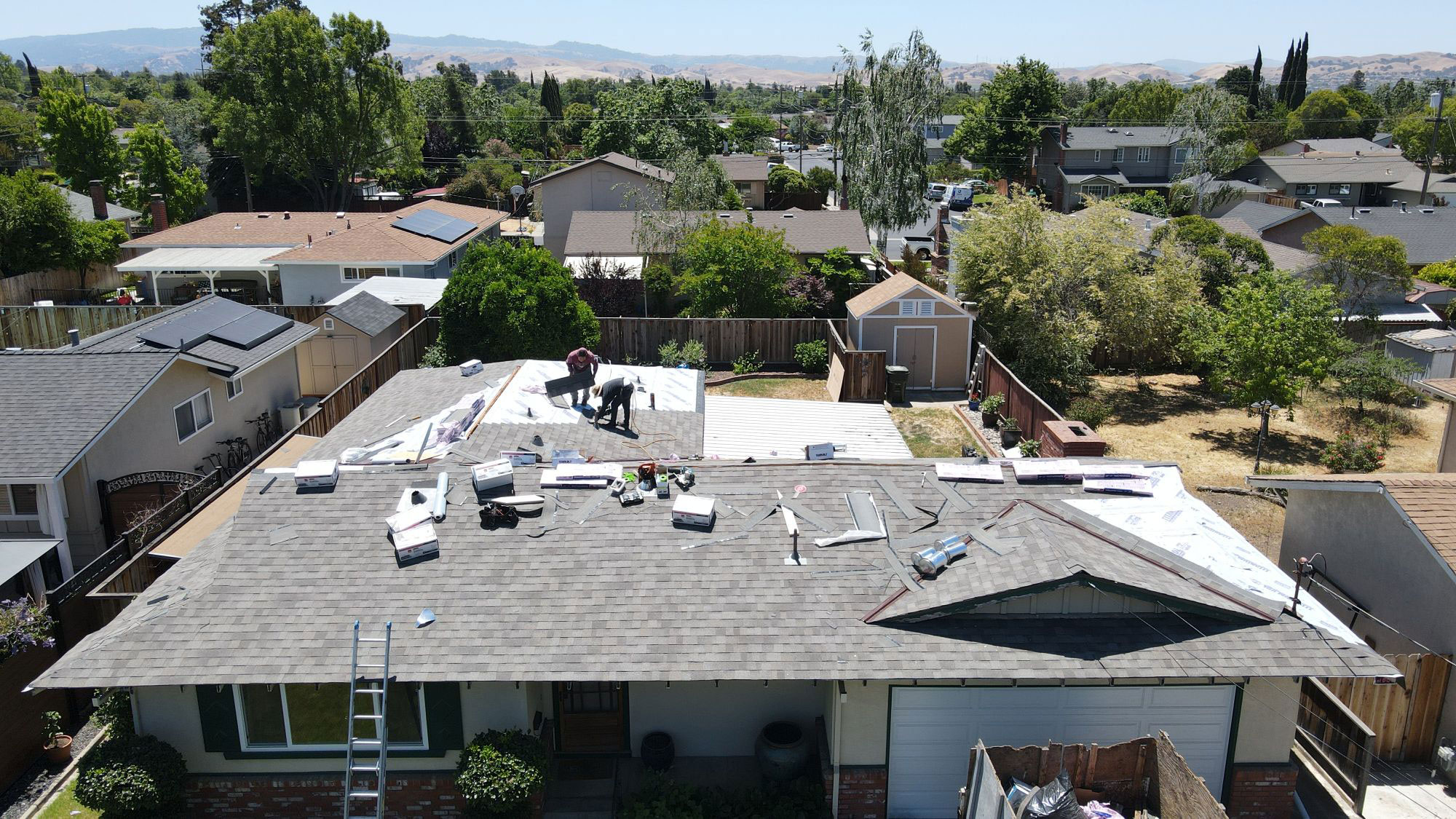 The image shows a residential house undergoing roof renovation, with visible construction materials and a partially completed roof structure.