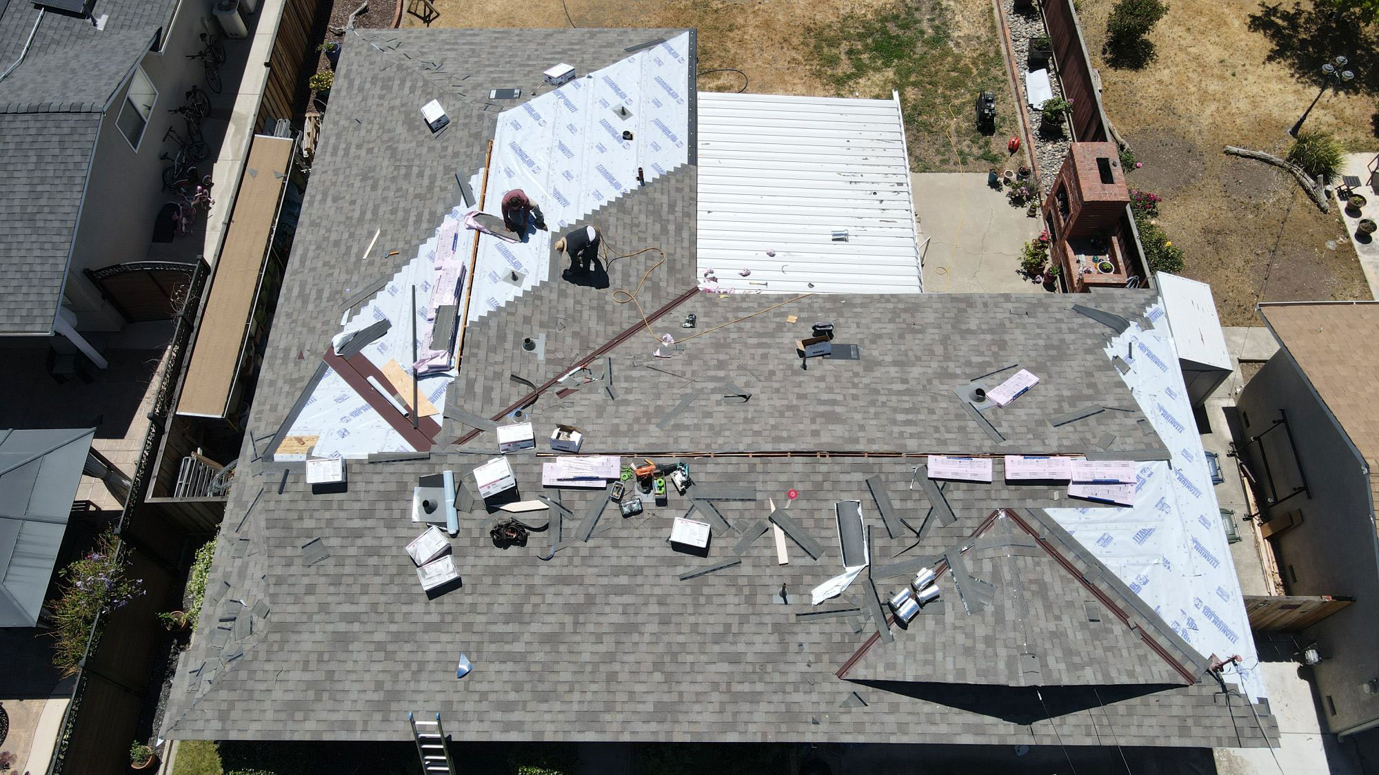 The image shows a roof under construction with exposed wooden beams and various materials scattered across the surface.