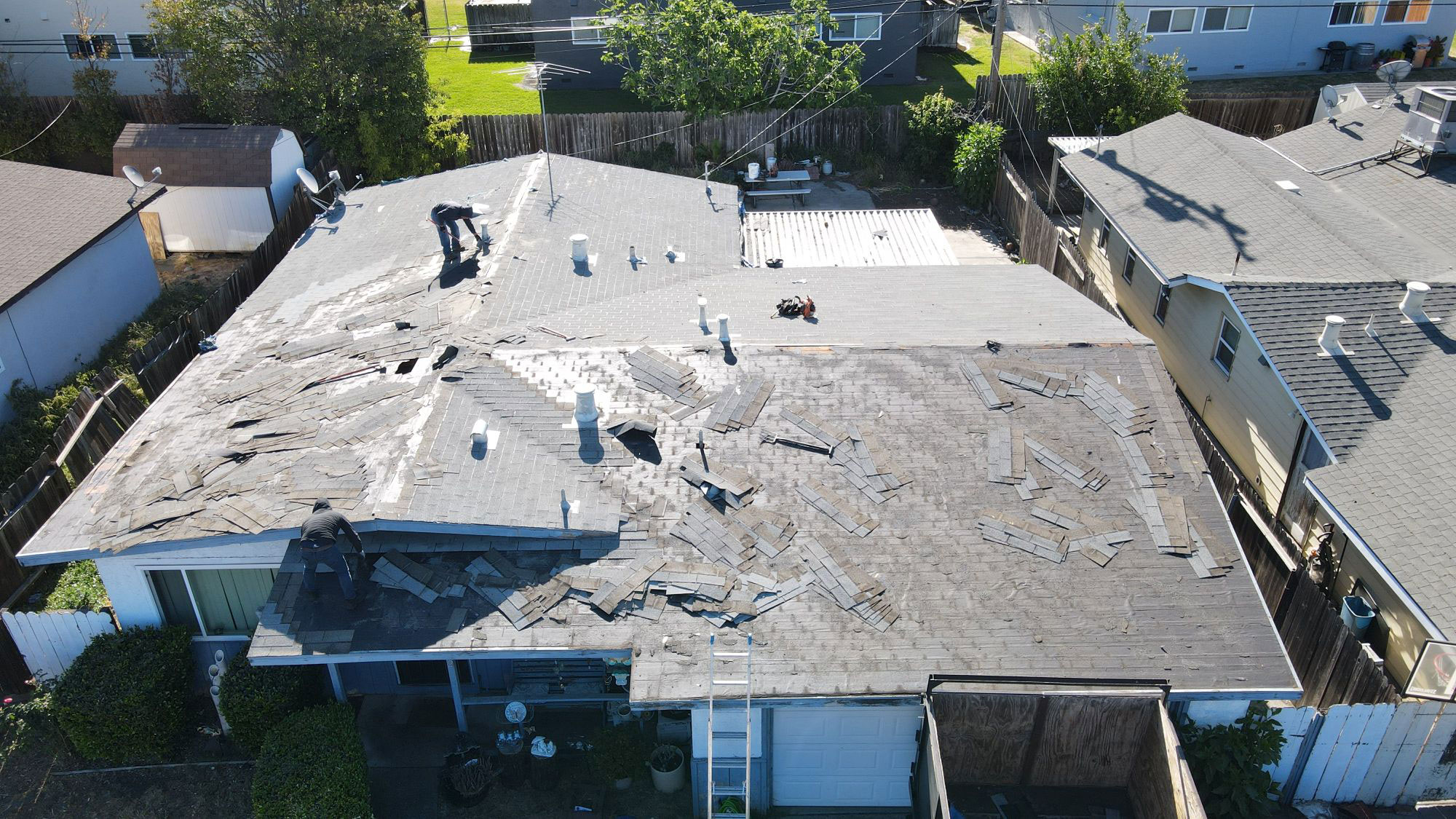 The image depicts a residential property with a damaged roof undergoing repair work.