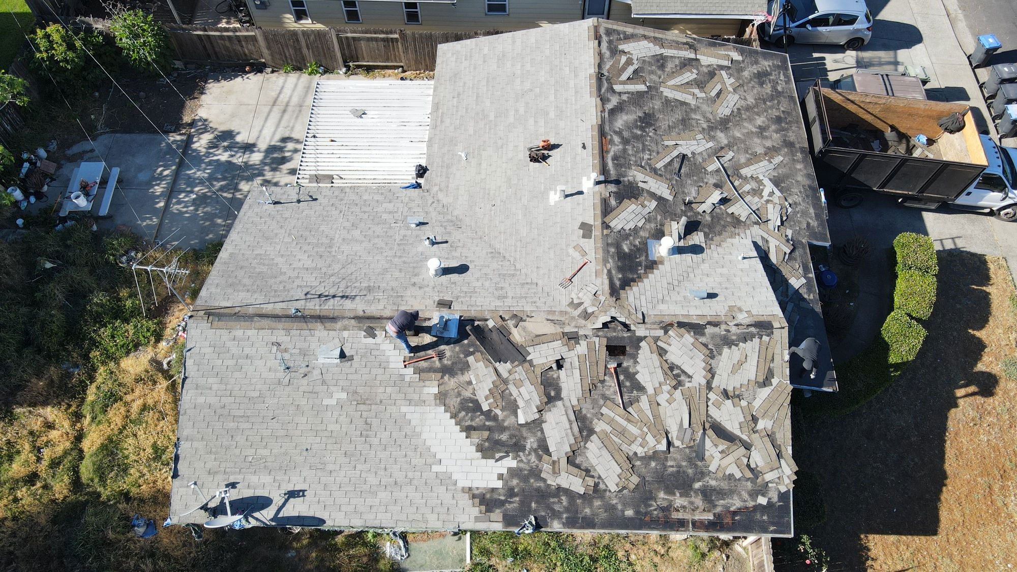 The image shows a building with a damaged roof undergoing repairs, featuring visible shingles being replaced and a partially open structure.