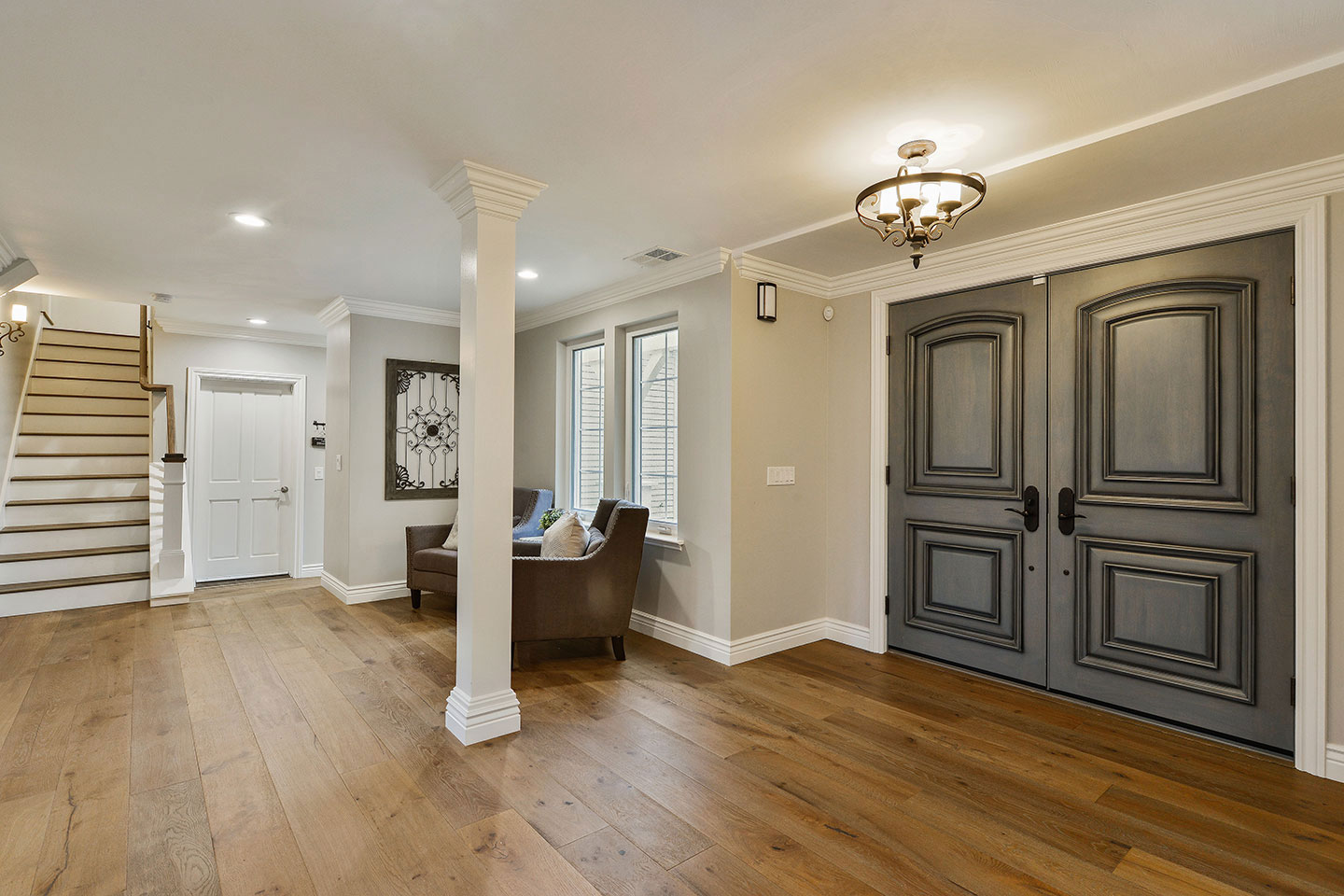 The image shows an interior view of a well-lit living room with hardwood flooring, a staircase leading upstairs, and a modern kitchen area visible in the background.