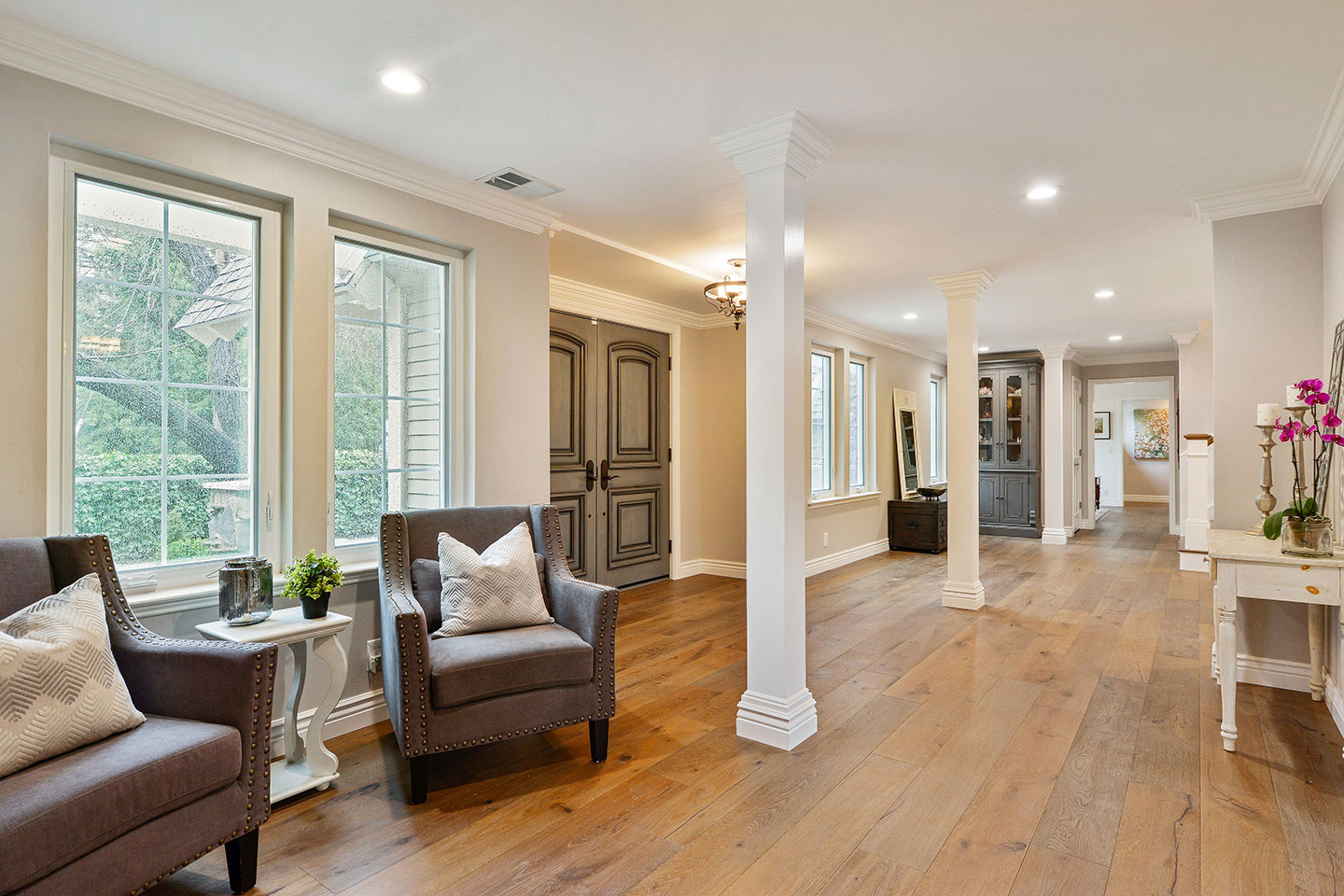 The image shows a spacious, well-lit living room with hardwood floors, white walls, and modern furniture.