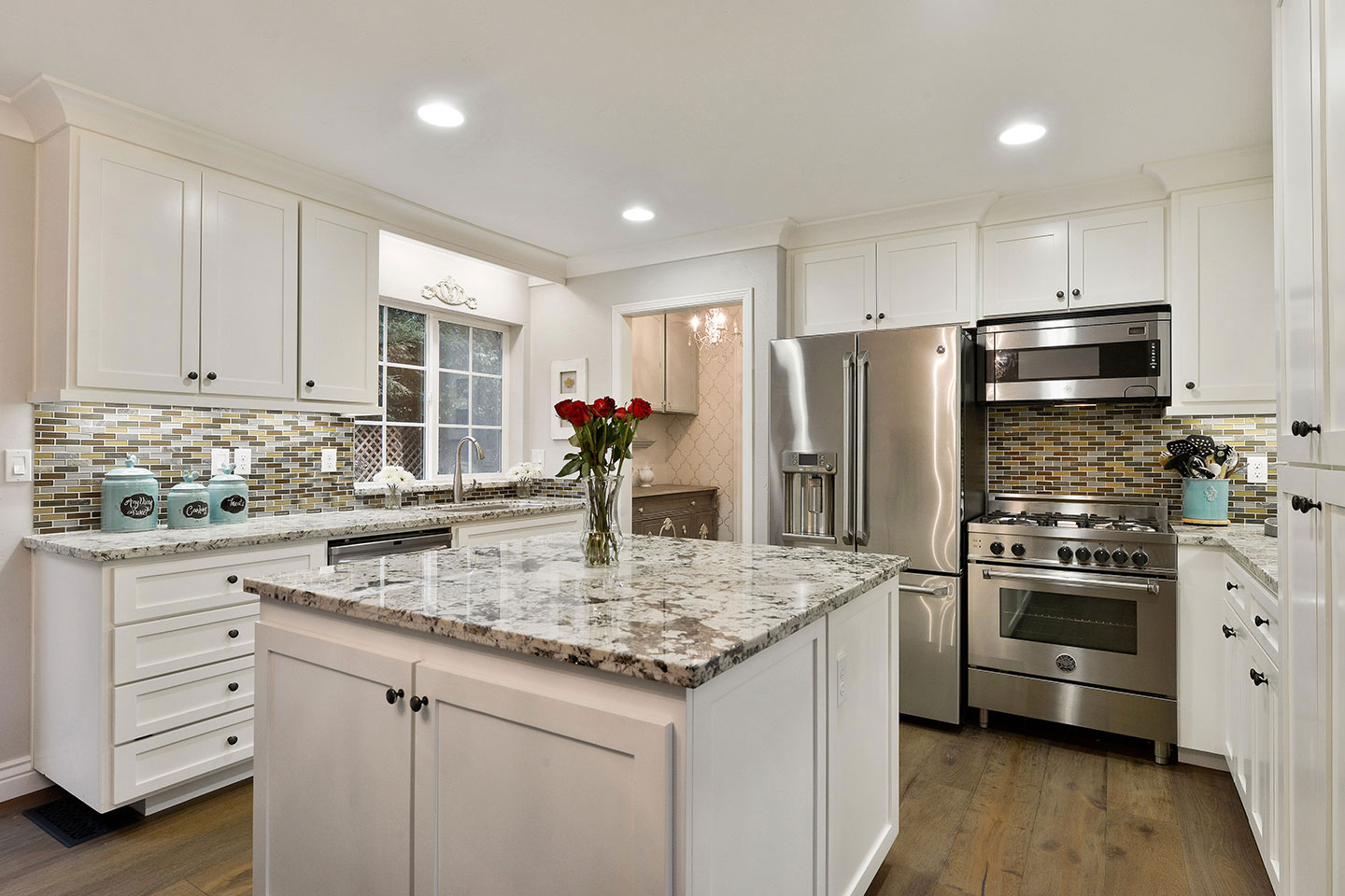 This is an interior kitchen scene featuring a modern design with white cabinets, granite countertops, stainless steel appliances, and marble backsplash.