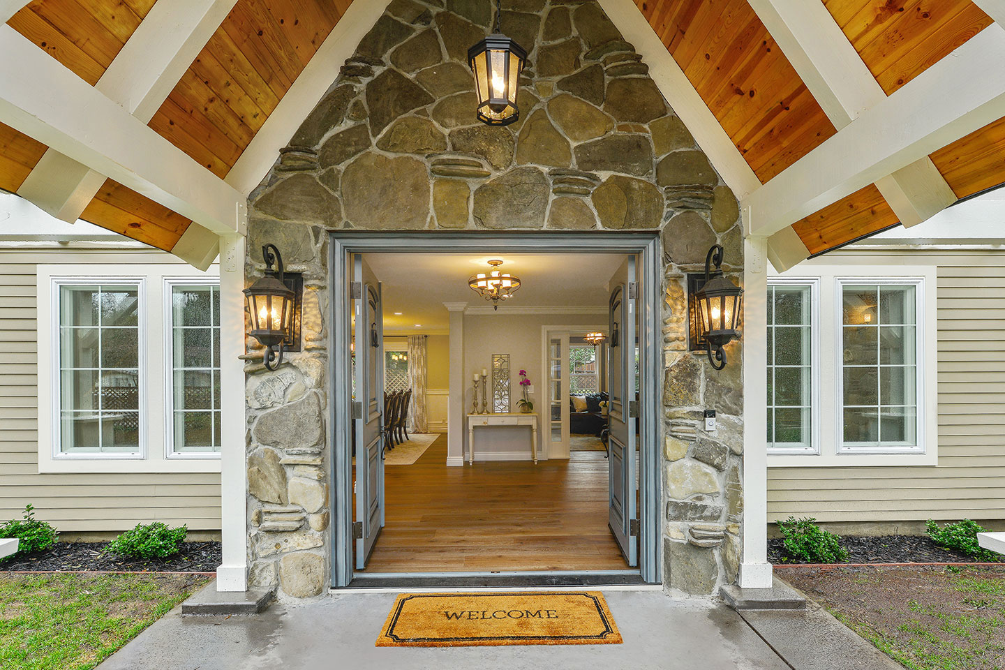 A large stone entranceway with a gabled roof and wooden beams, leading to a building with a covered porch and a welcoming atmosphere.