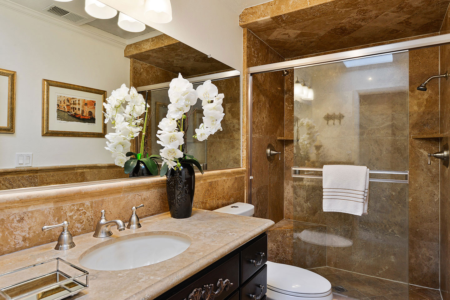 The image shows a luxurious bathroom with a marble-tiled floor and walls, a double sink vanity, a walk-in shower, and a modern design aesthetic.