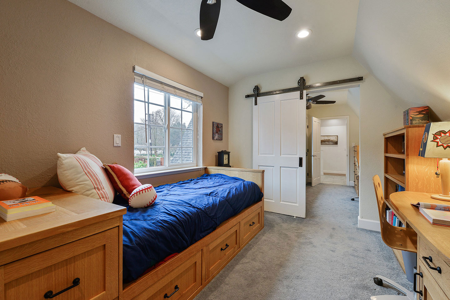 The image shows a well-lit bedroom with a neatly made bed, a desk area, a built-in closet, and a ceiling fan.