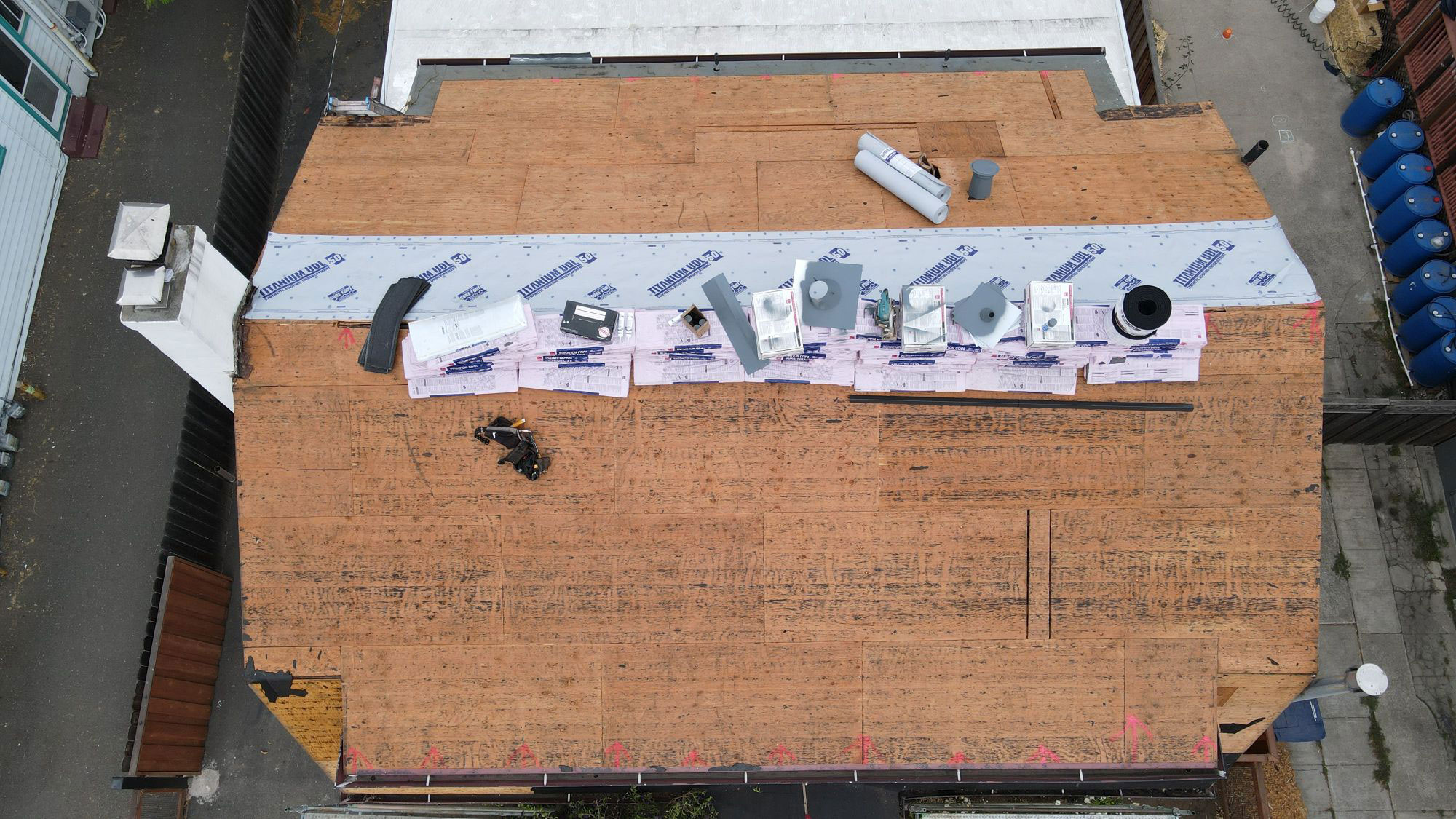 The image shows a building with a roof under construction or repair, featuring exposed wooden decking and various materials placed on top, possibly for renovation or installation purposes.