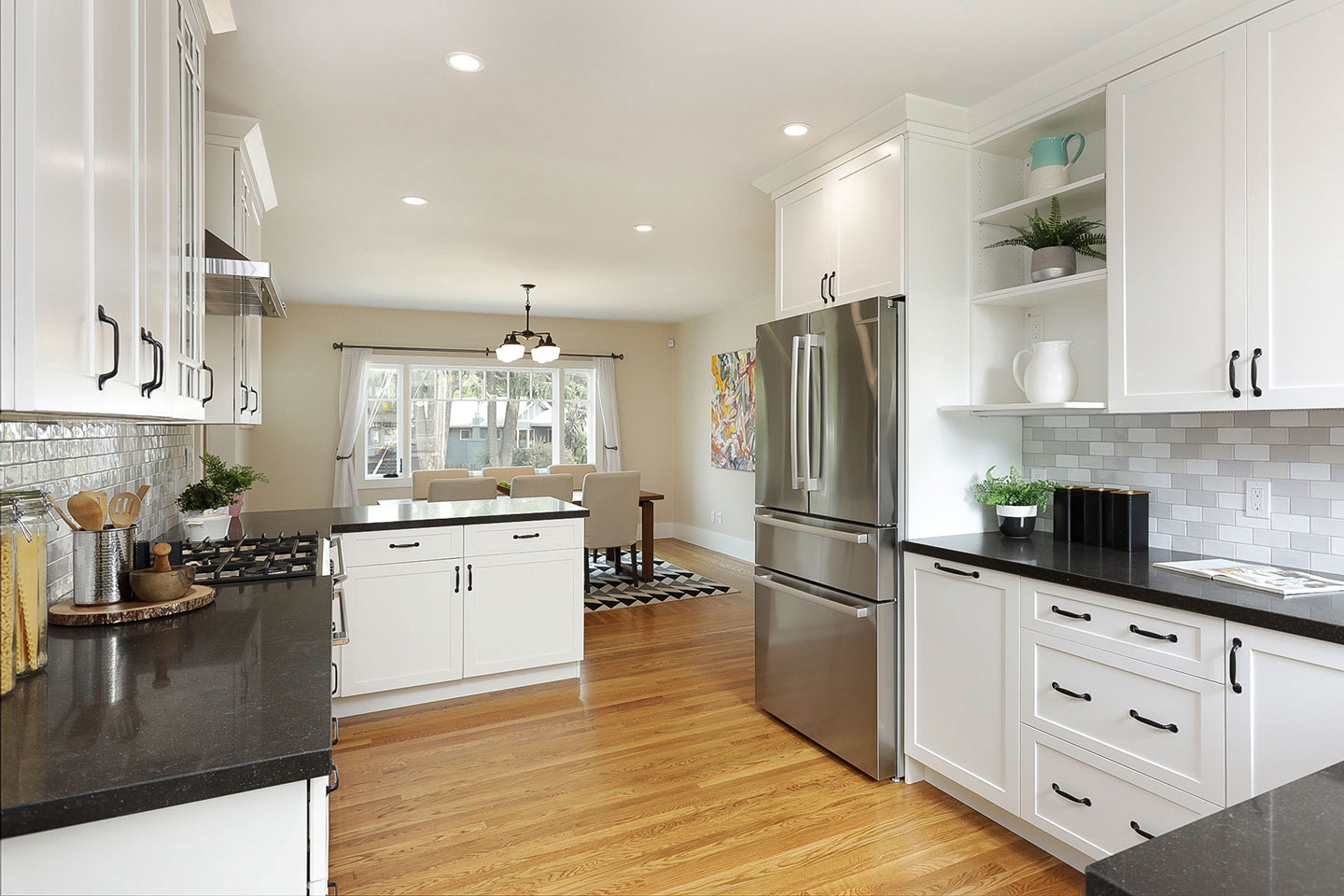 Modern kitchen with white cabinets, stainless steel appliances, black countertops, and hardwood floors.
