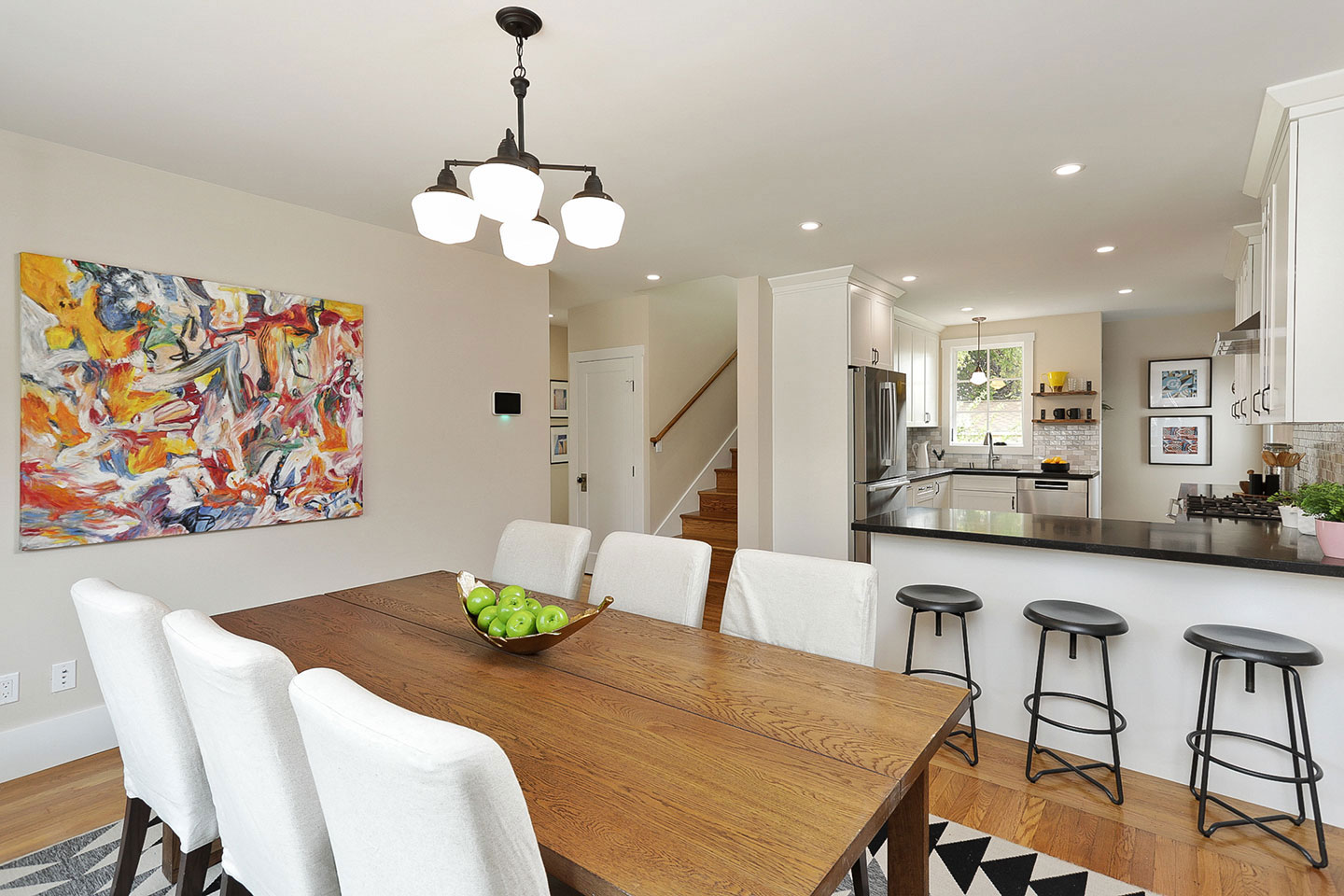 The image shows an interior space with a modern kitchen and dining area, featuring a large island countertop, cabinetry, and contemporary furniture including chairs and a table.