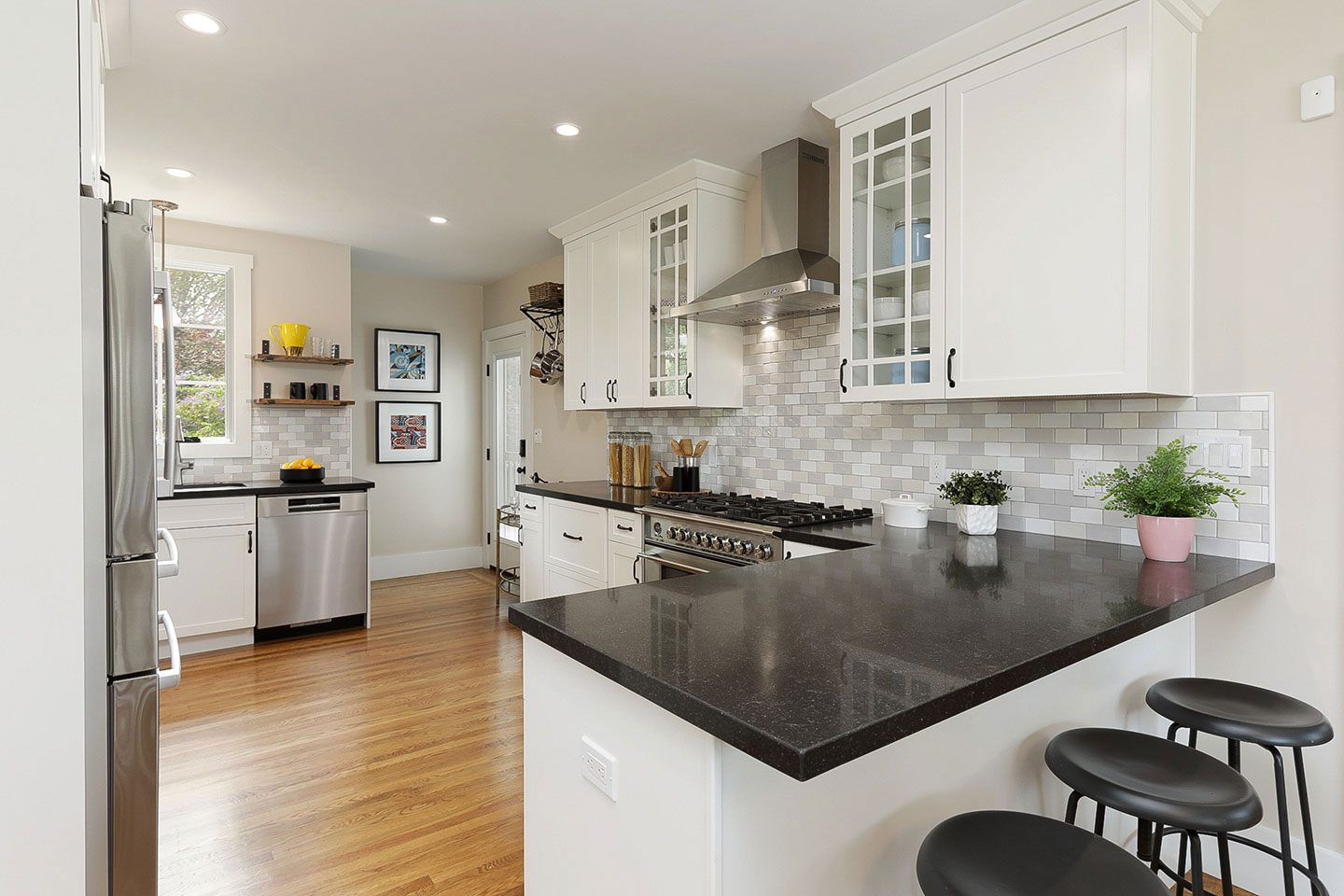 The image displays a modern kitchen interior with a dark granite countertop, white cabinets, stainless steel appliances, and a black island with barstools.