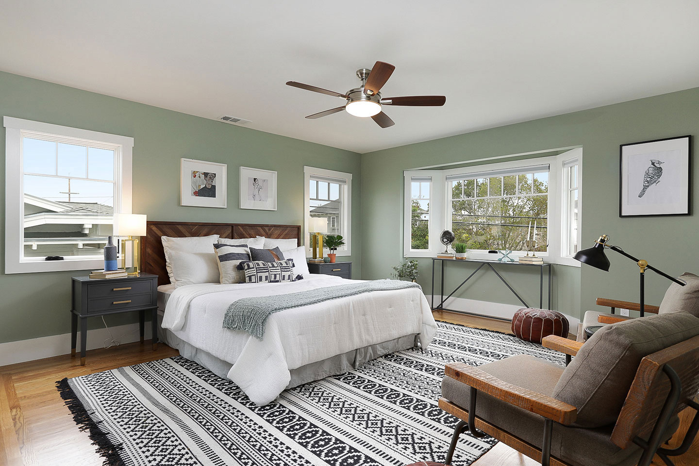 The image shows a neatly arranged bedroom with a large bed, patterned rug, wooden furniture, and decorative items on a clean wall.
