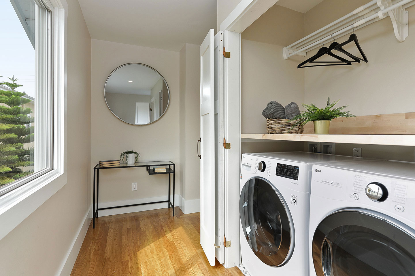 The image displays a modern, well-lit laundry room with a washing machine and dryer, set against a backdrop of a window with natural light streaming in.