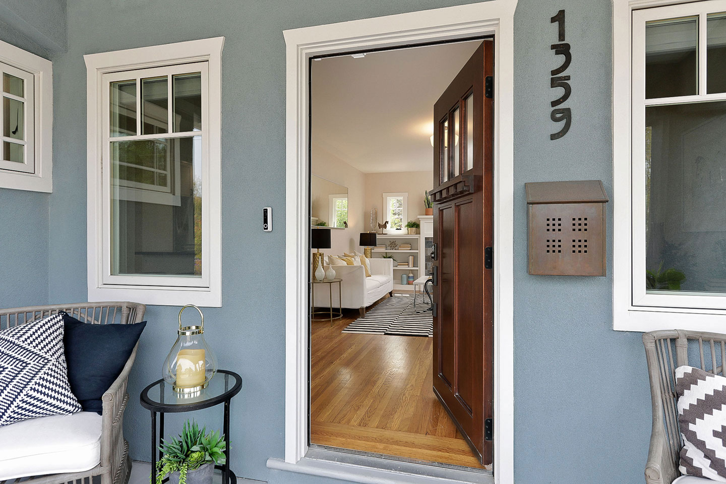 The image shows an exterior view of a house with a prominent front door, a porch, and a living room visible through the glass panels of the door.