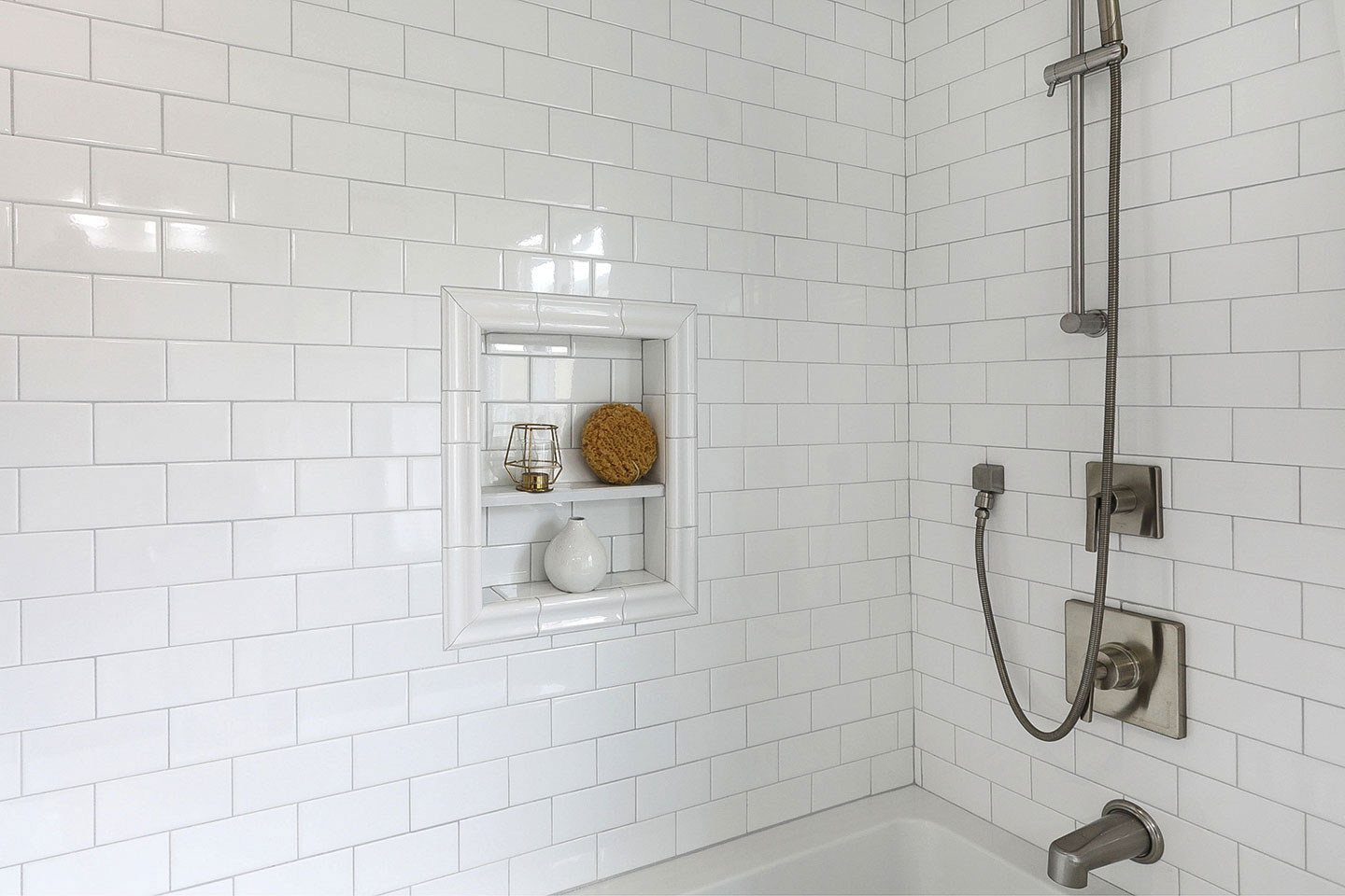 The image shows a modern bathroom with white tiles, featuring a shower stall with a clear glass door, a wall-mounted faucet, and a white towel hanging on a rack.