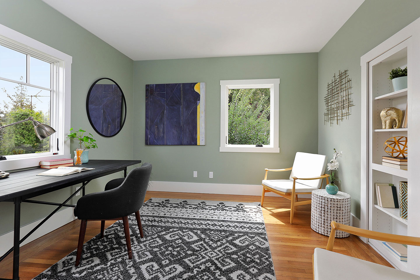 An interior room with a modern design, featuring a desk, chair, rug, window, bookshelf, and decorative elements.