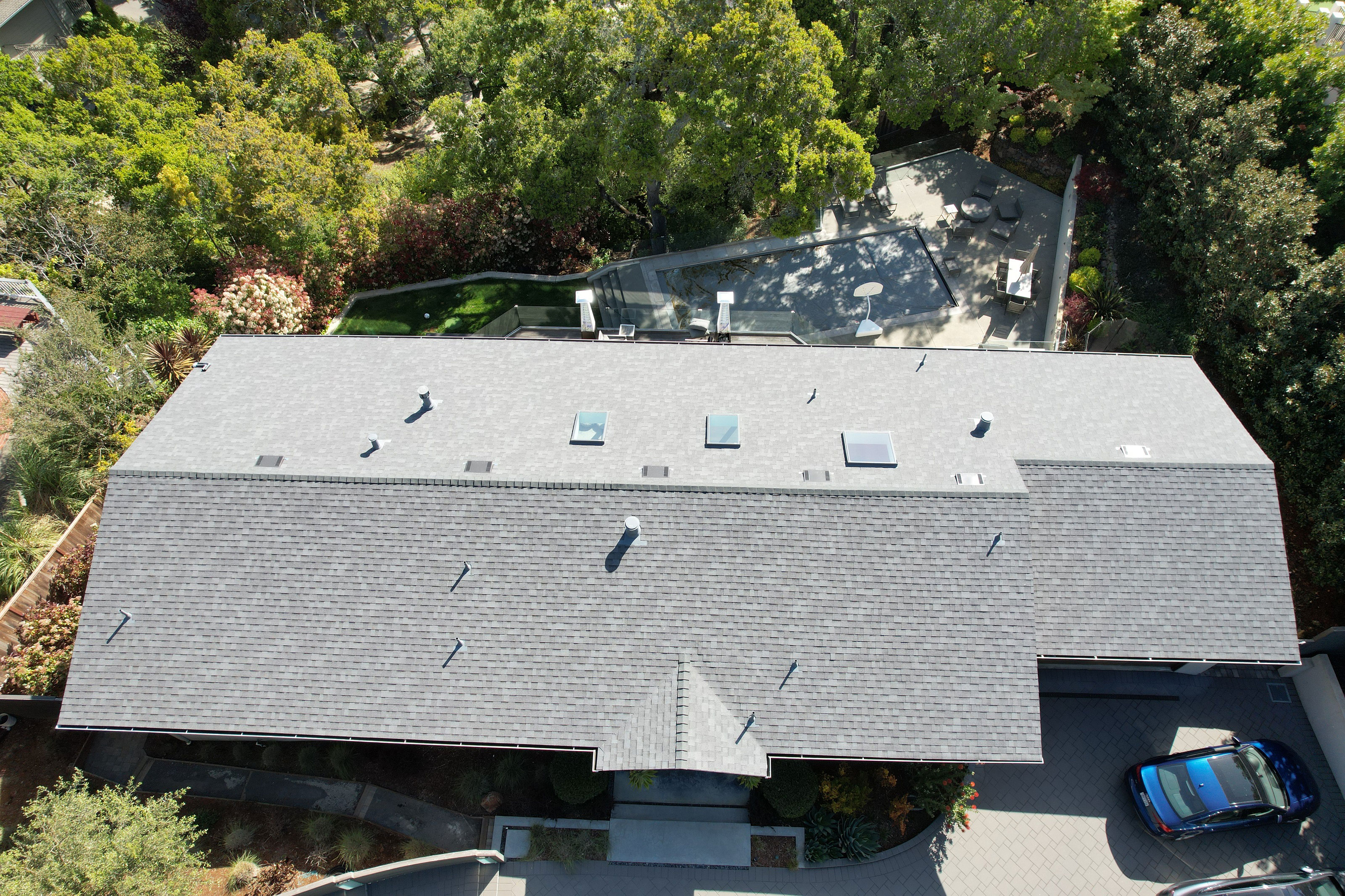 The image shows a modern two-story residential house with a flat roof, visible solar panels, and a covered carport.