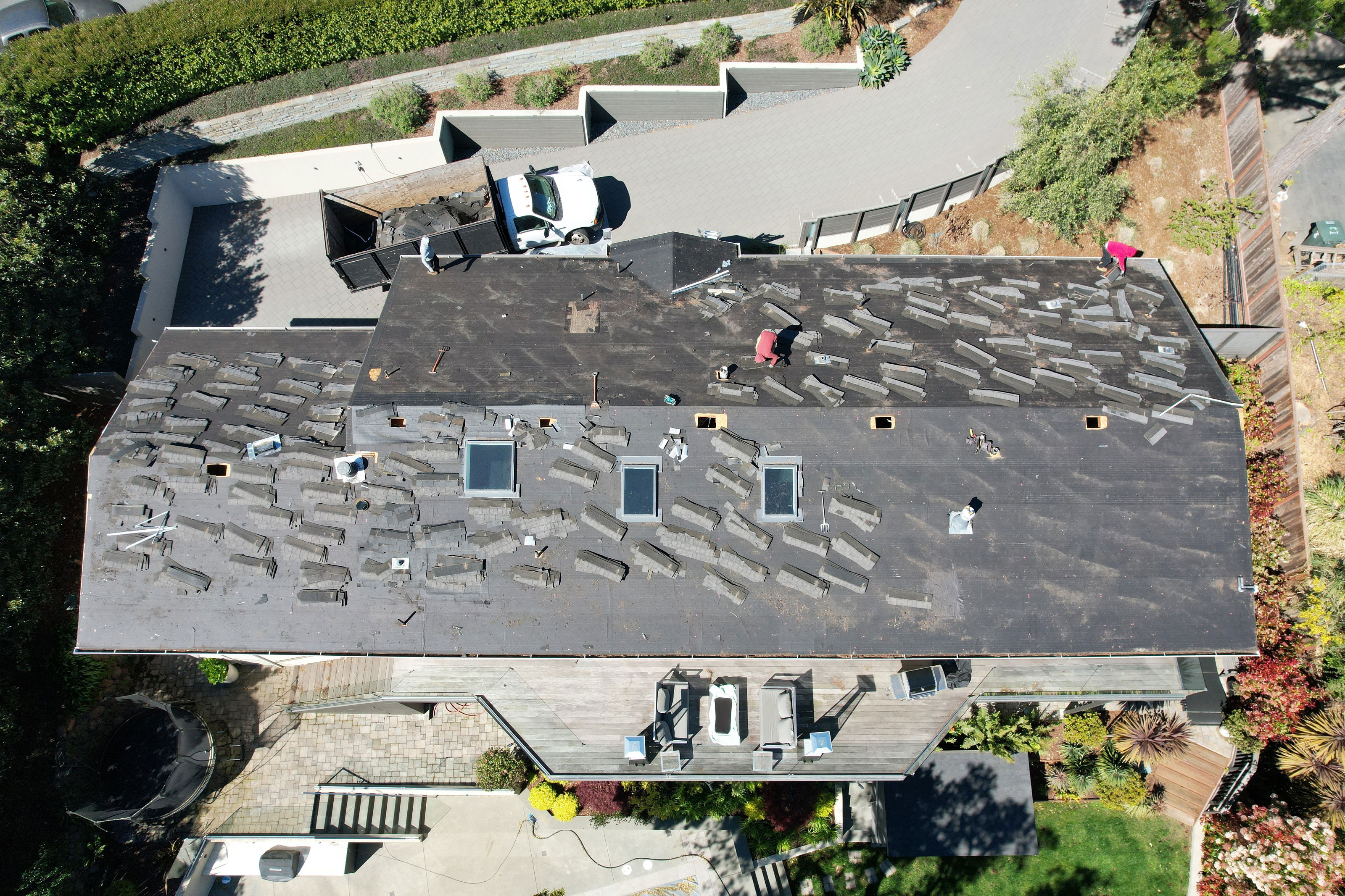 The image shows a building with a flat roof covered in black shingles, which appears to be undergoing repair work, as evidenced by the exposed areas of the roof and the presence of construction materials.