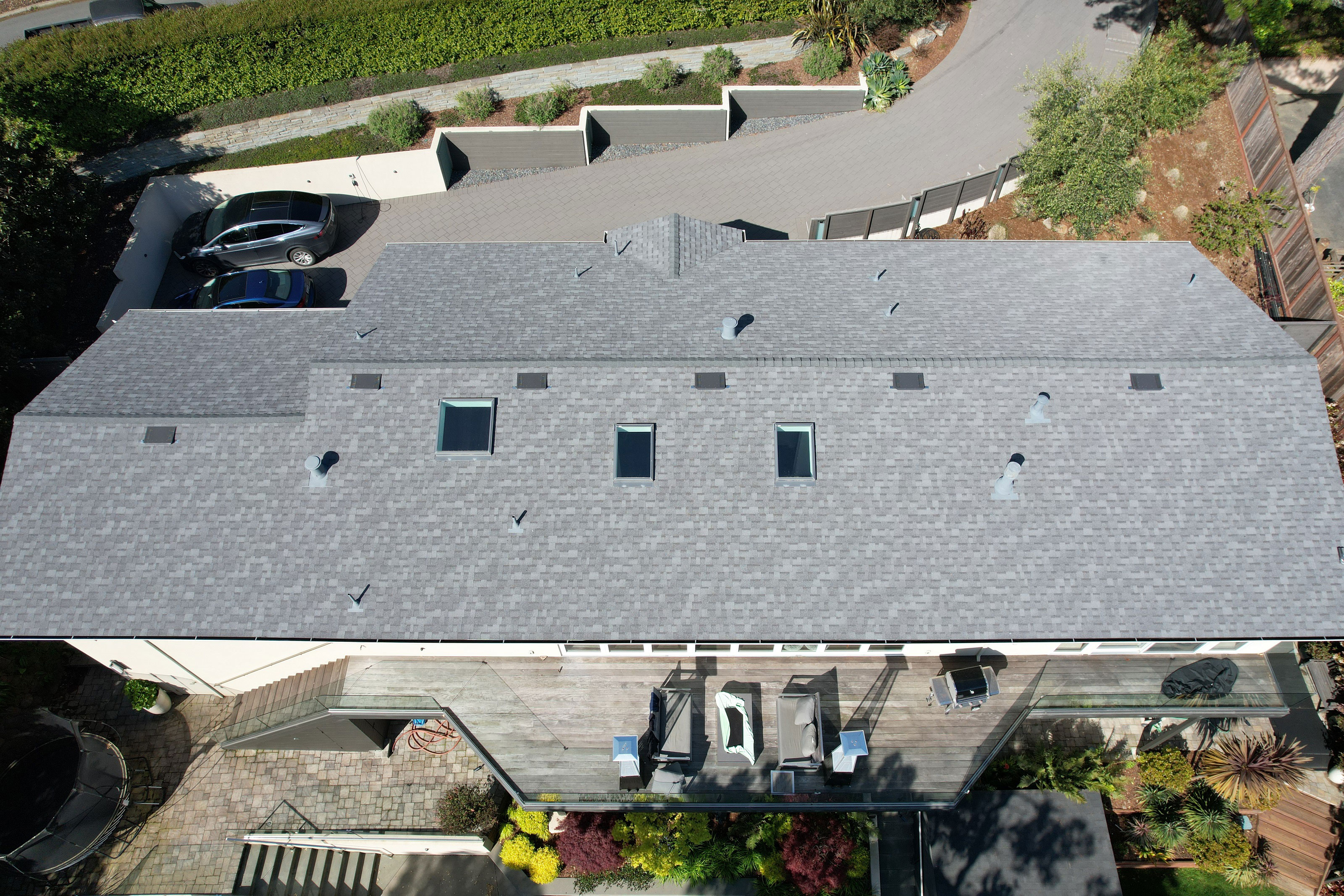 The image shows a two-story residential house with a gray shingle roof, a prominent front gable, and a garage on the left side.