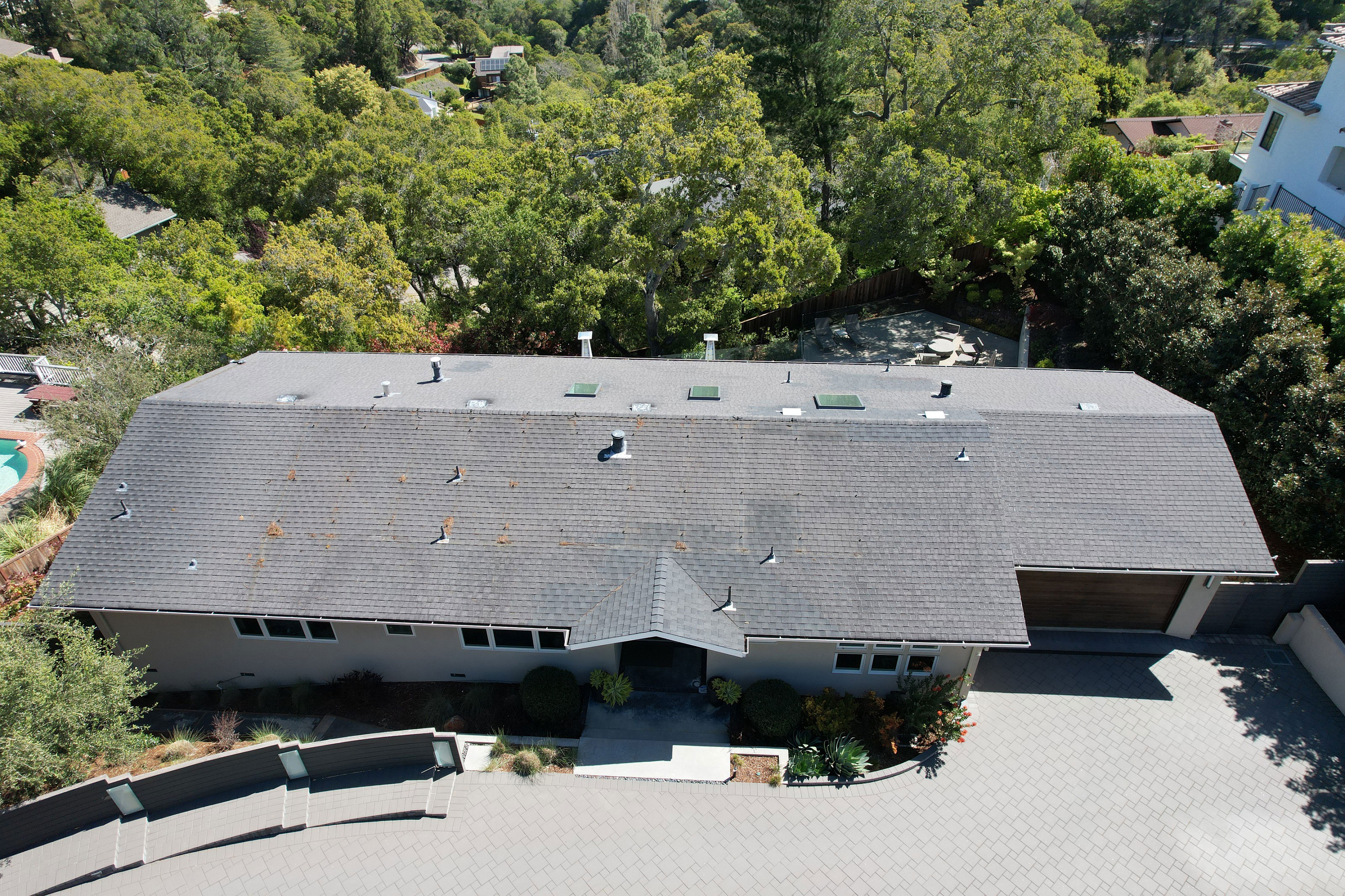 The image shows a two-story residential house with a flat roof, situated on a street with trees and other houses visible in the background.