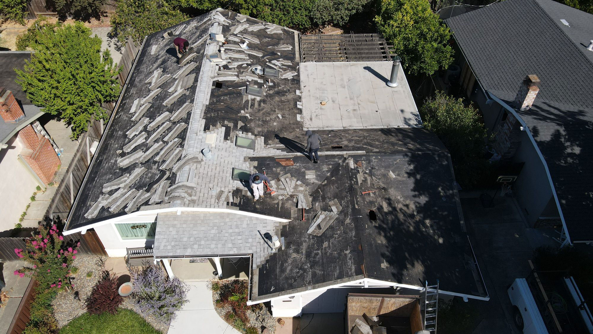 The image shows a house with a damaged roof undergoing repair work, featuring visible shingles missing and exposed areas where new materials are being installed.
