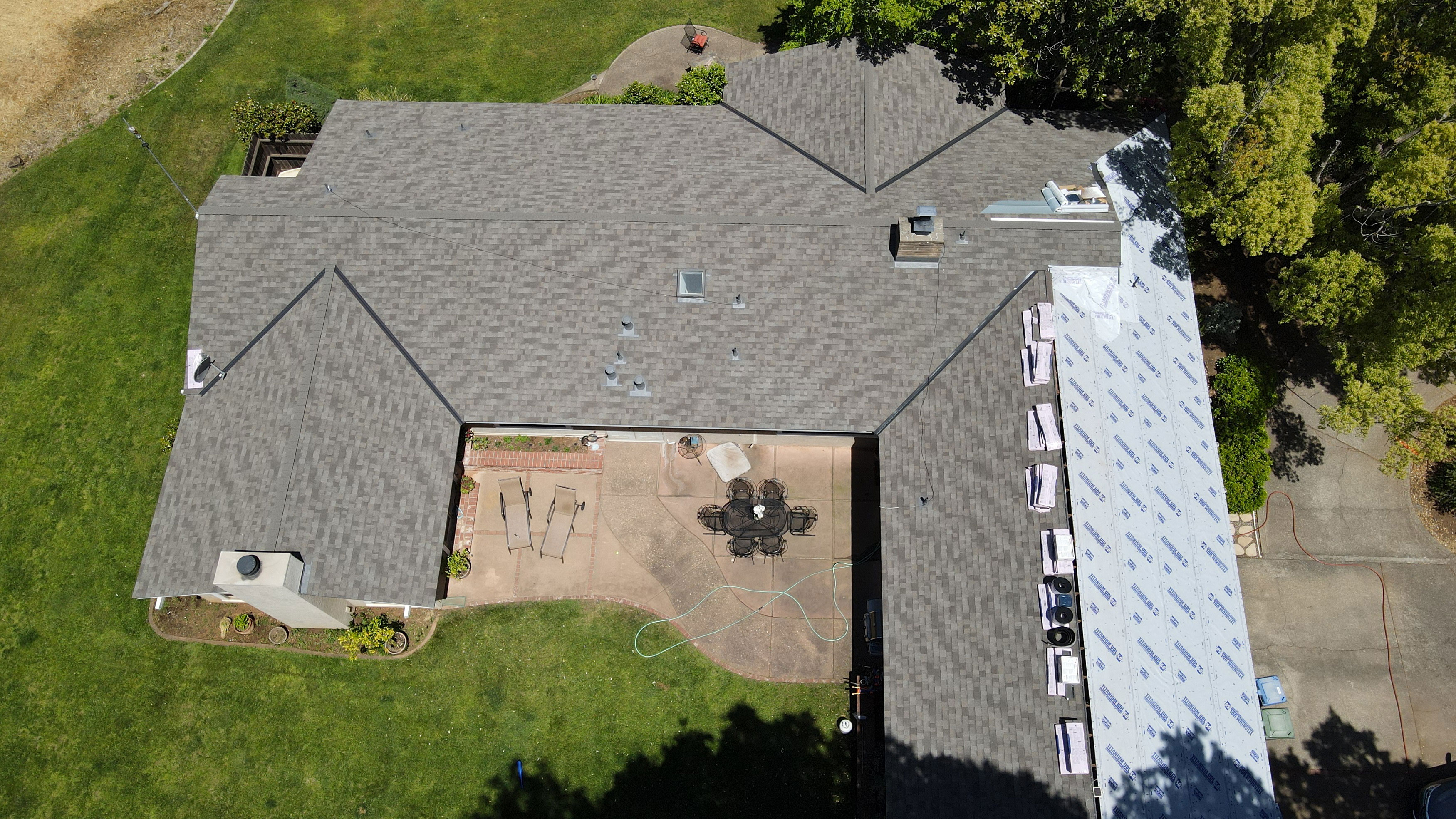 The image depicts a residential house under construction with visible roofing materials and a partially covered backyard area.