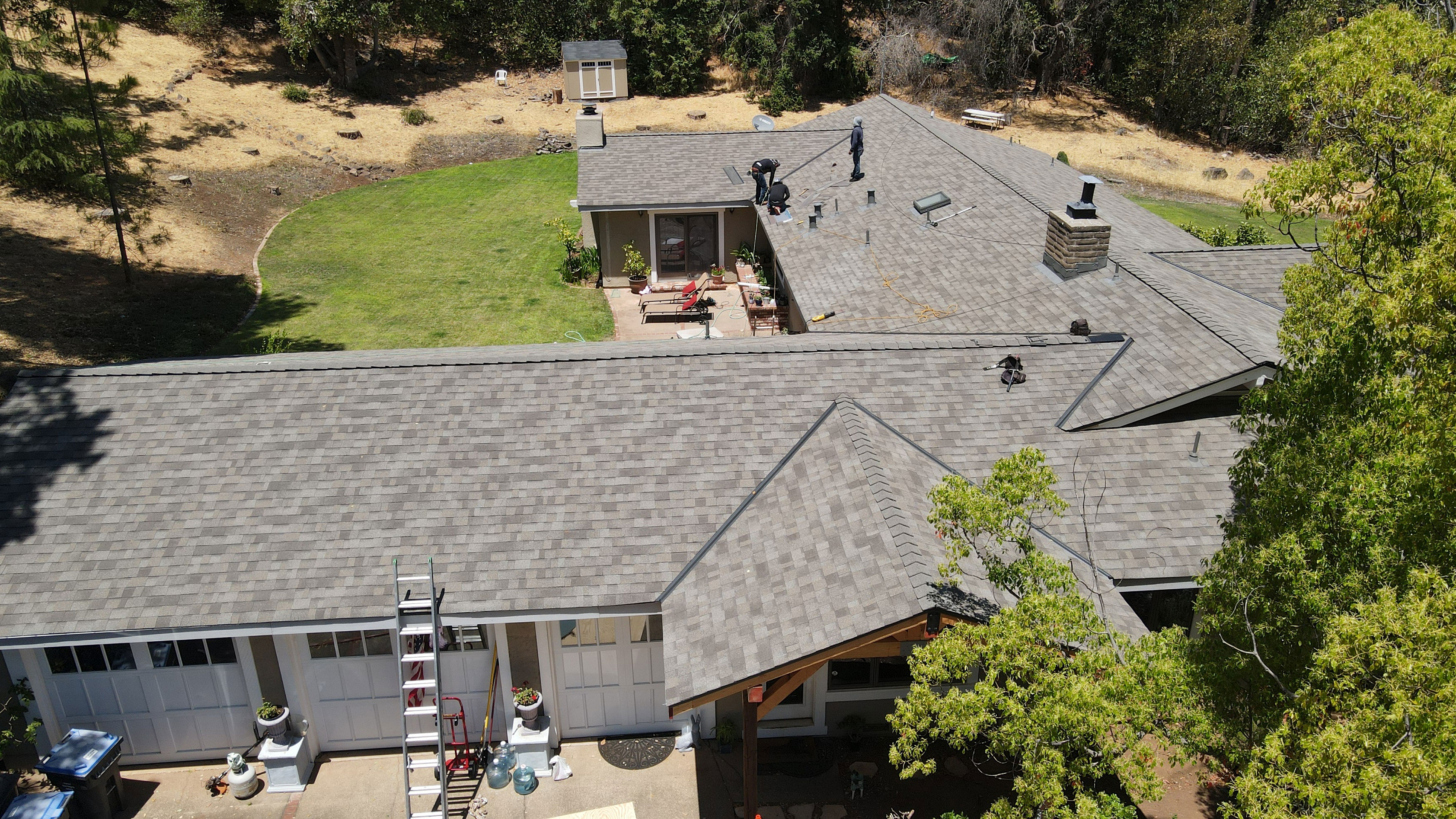 The image shows a residential house with a shingled roof under a clear sky, viewed from an elevated angle.
