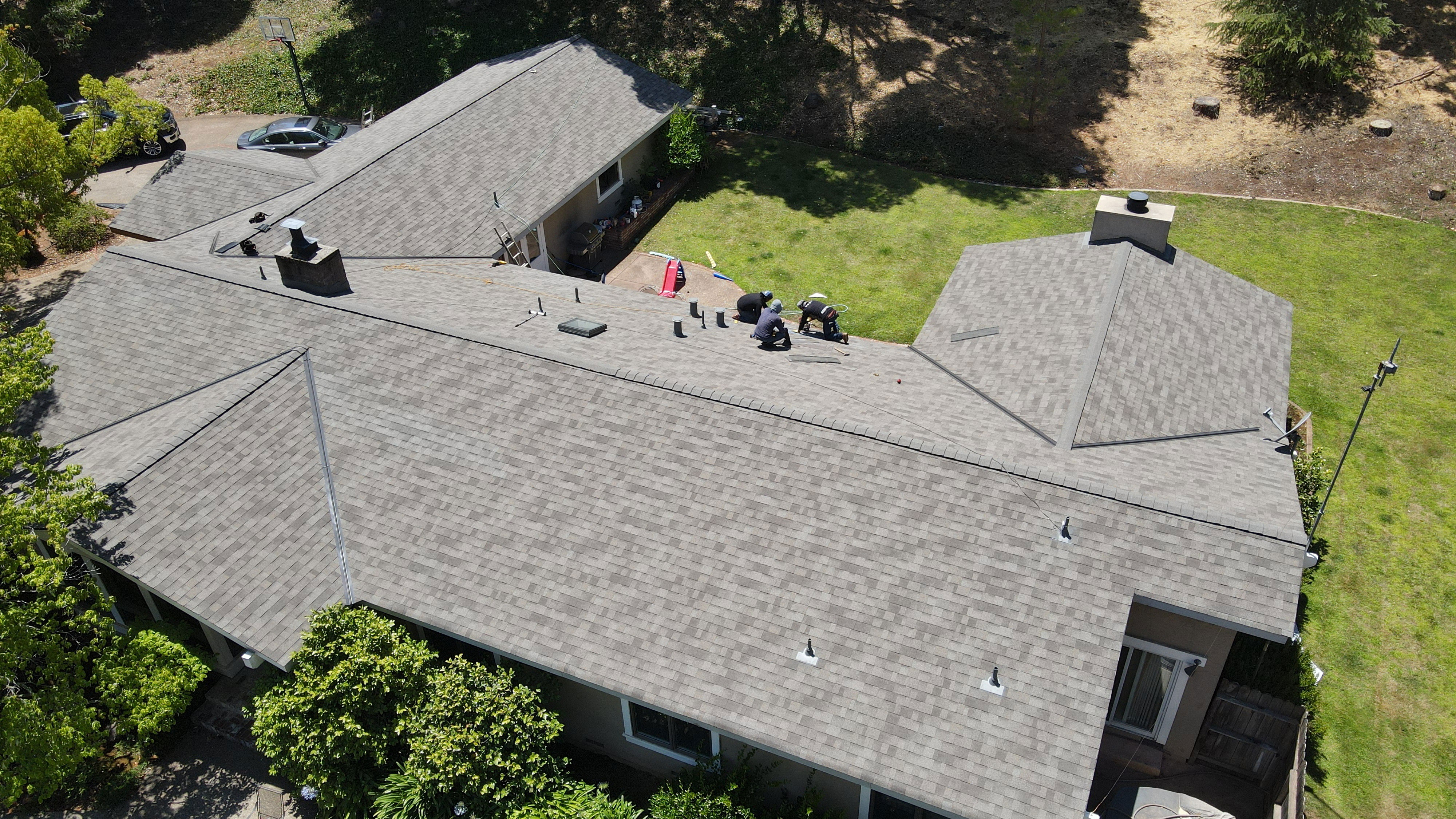 The image shows a residential house with a gray shingle roof, a well-maintained lawn, and a clear sky above.