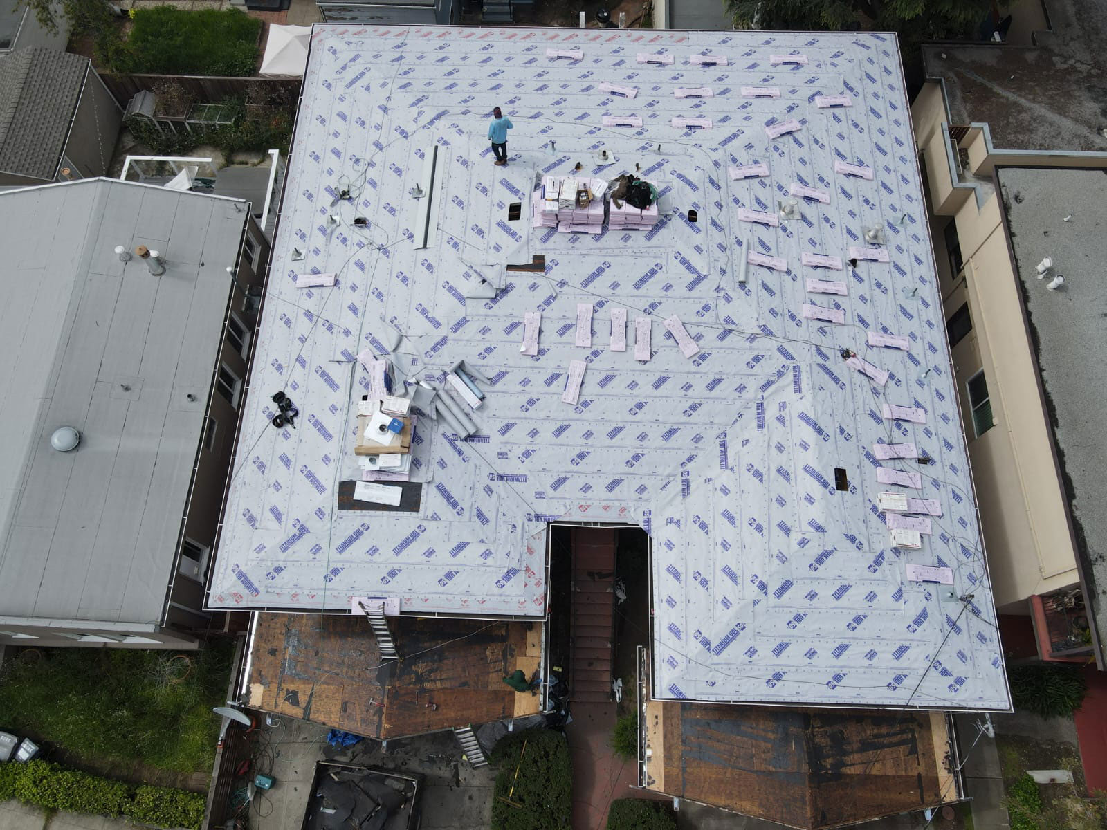 The image shows a roof under construction with various materials and tools visible on it.