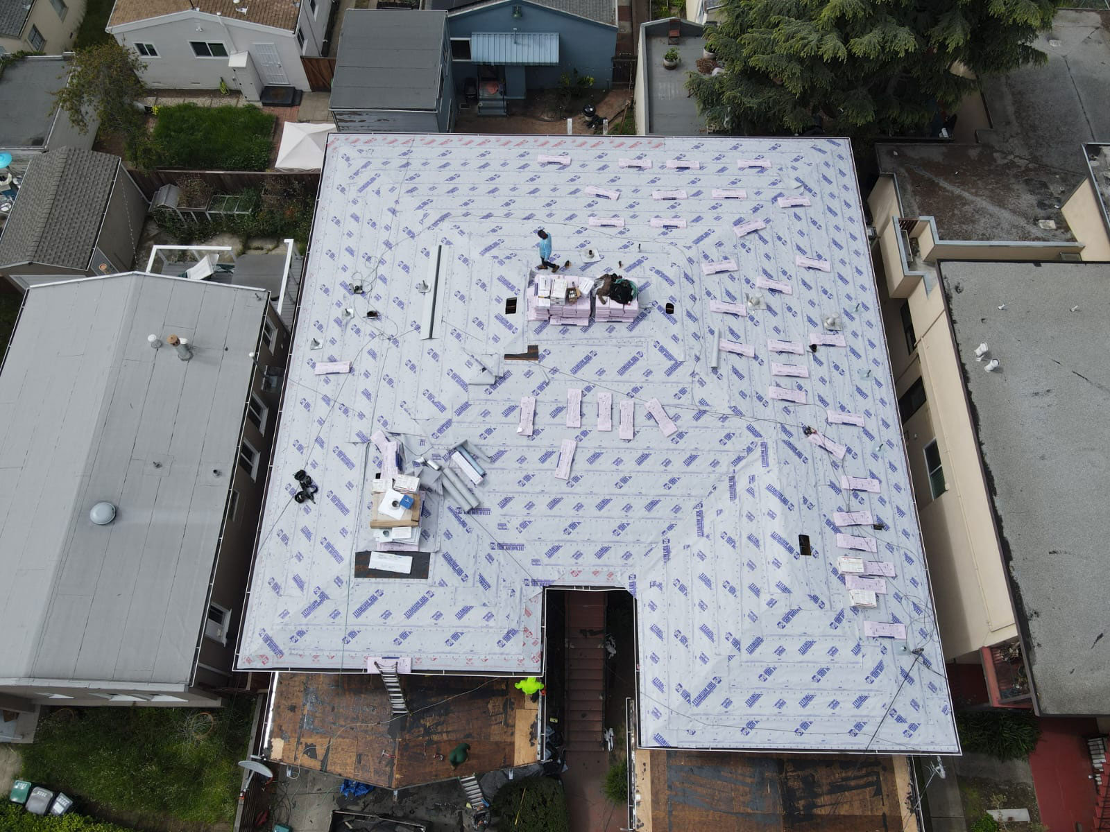 The image shows a residential building under construction with a visible tarp roof covering the unfinished structure.