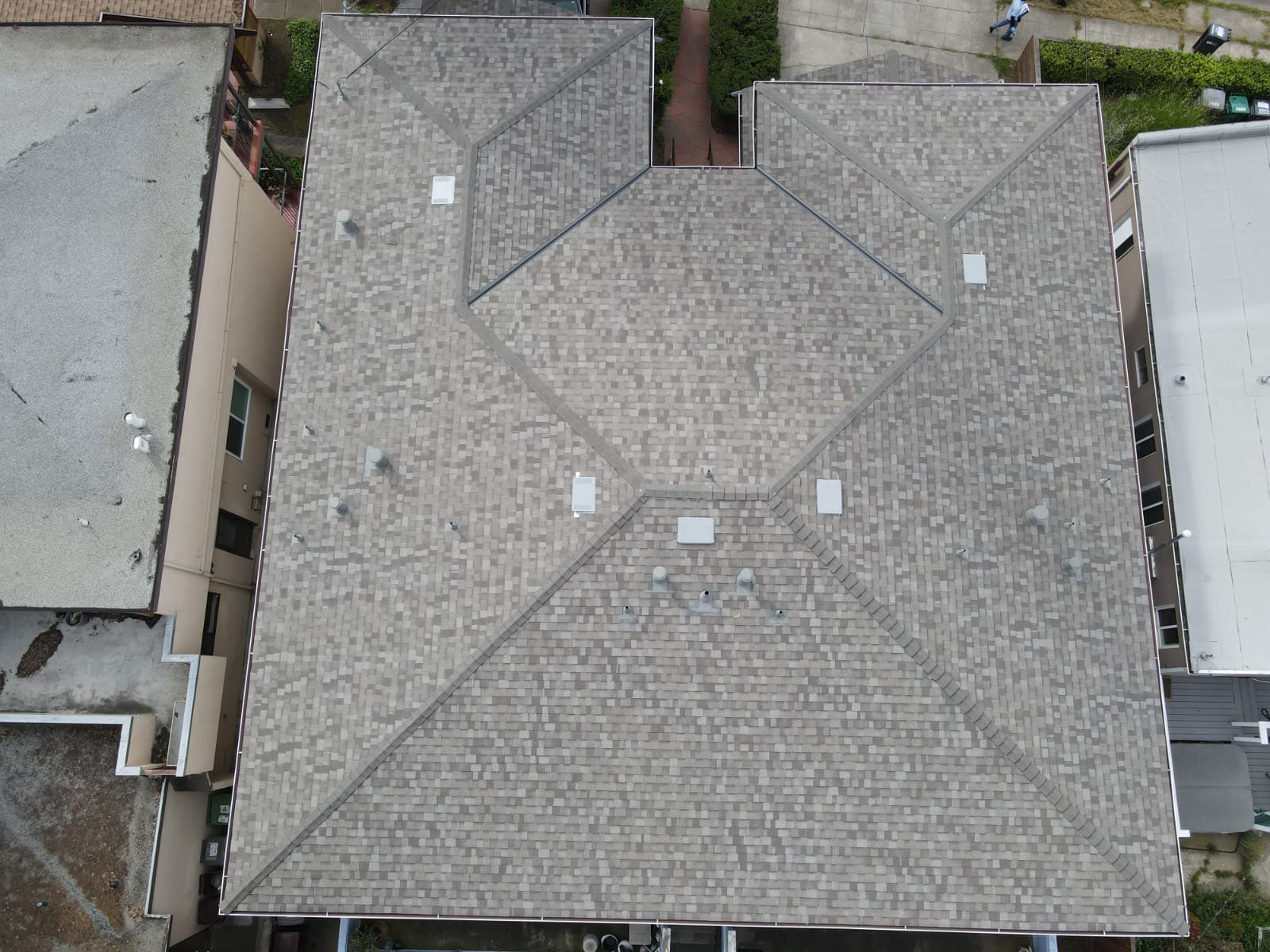 The image shows a flat roof with multiple skylights, taken from an angle that captures its architectural details against a backdrop of residential buildings.
