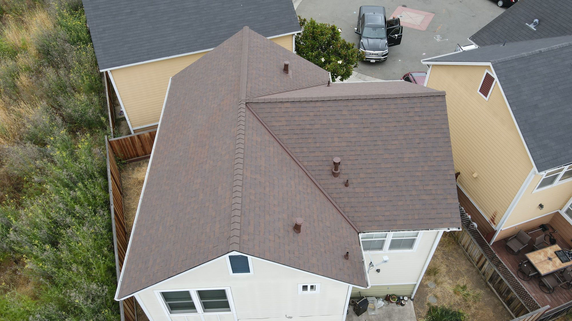 The image shows a residential house with a shingled roof and a brown exterior wall, viewed from an angle that captures part of the front yard and another adjacent house.