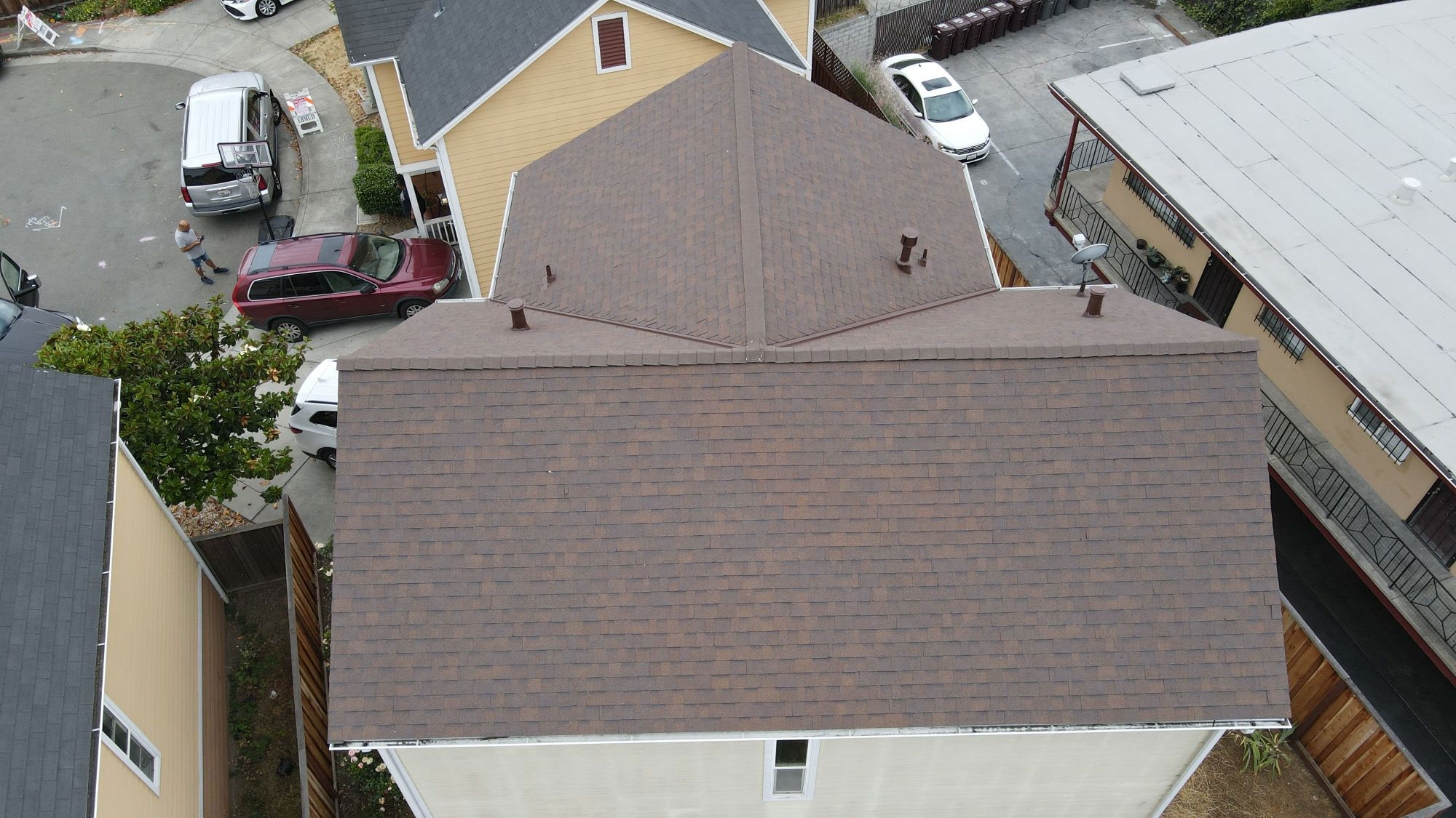 The image shows a residential area with a house under construction featuring a shingled roof and a partially visible garage door, photographed from an elevated angle.